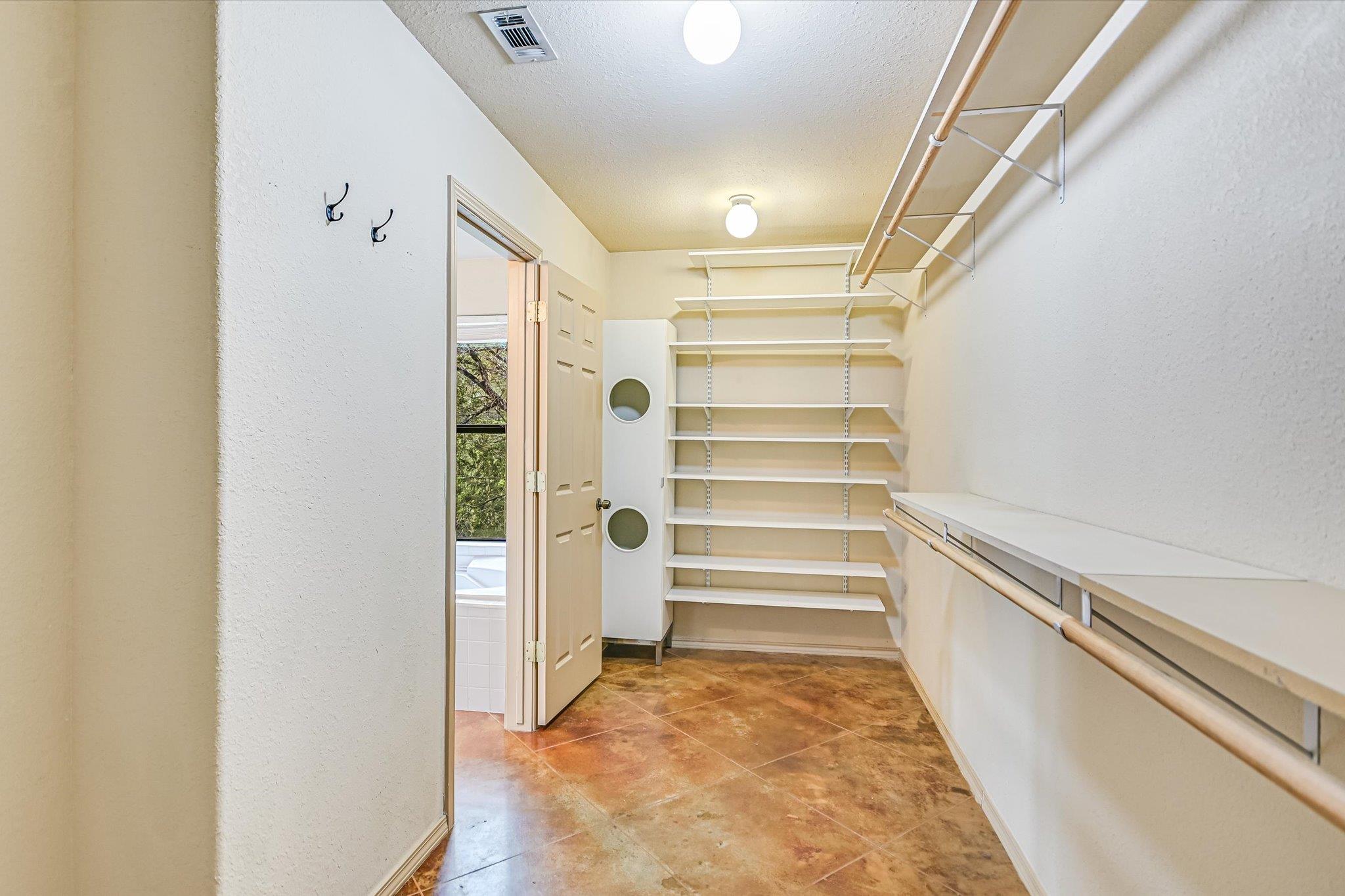 Walk-in closet with extensive shelving, hanging rods, and brown tile flooring.