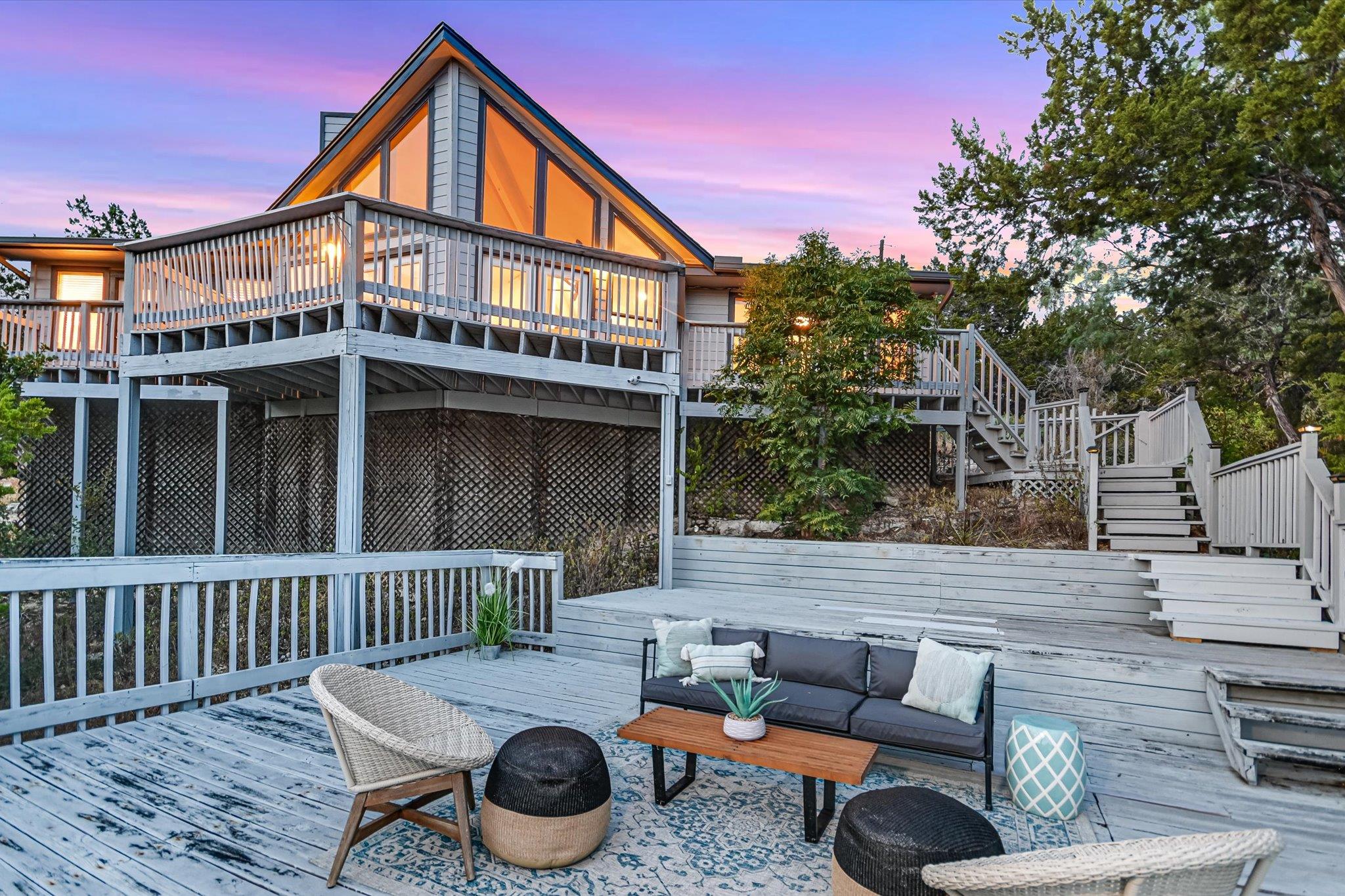 Elevated home with a triangular glass facade above a furnished multi-level deck at dusk.