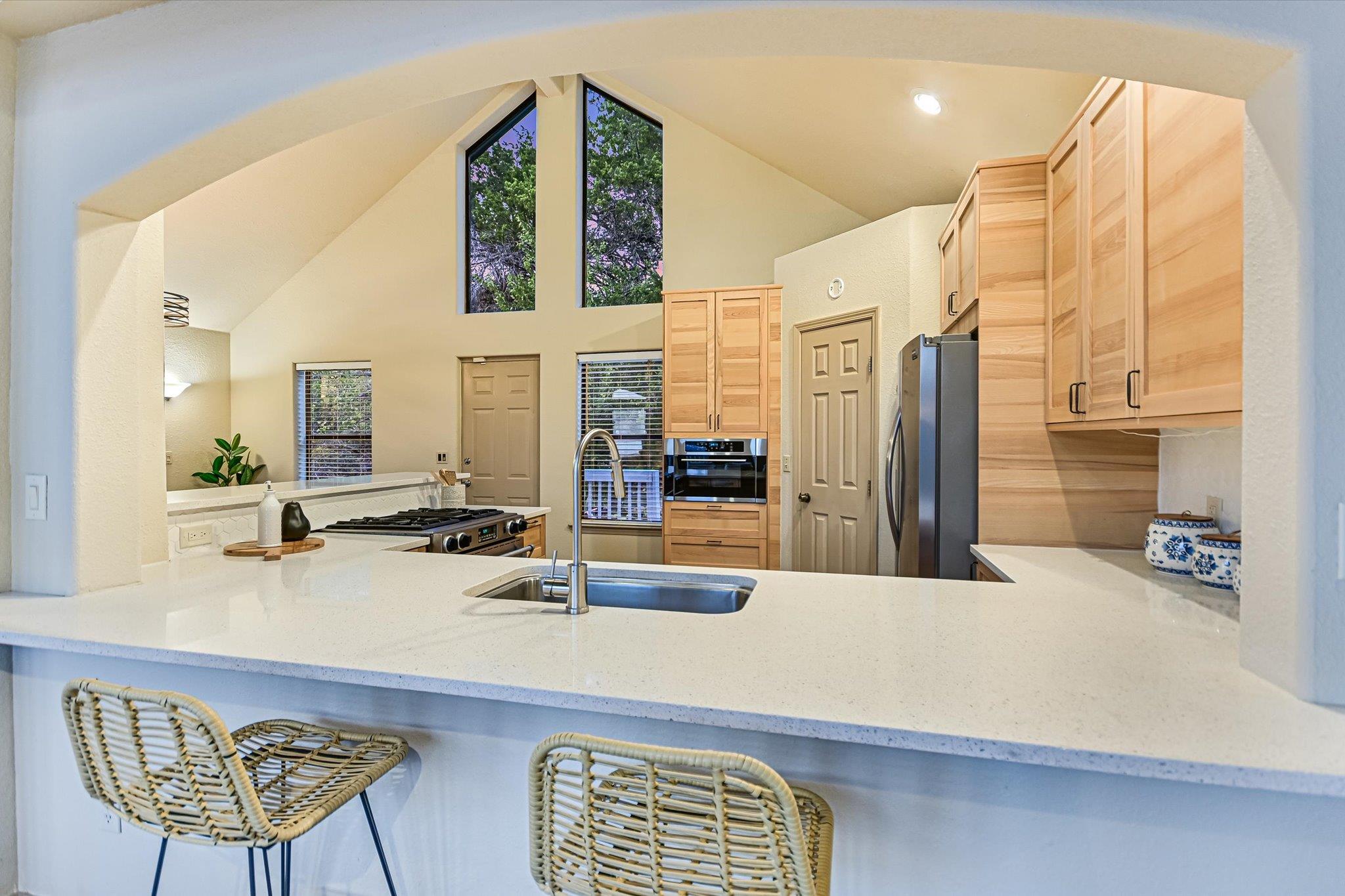 Kitchen with vaulted ceiling, light wood cabinets, white island, and stainless-steel appliances.