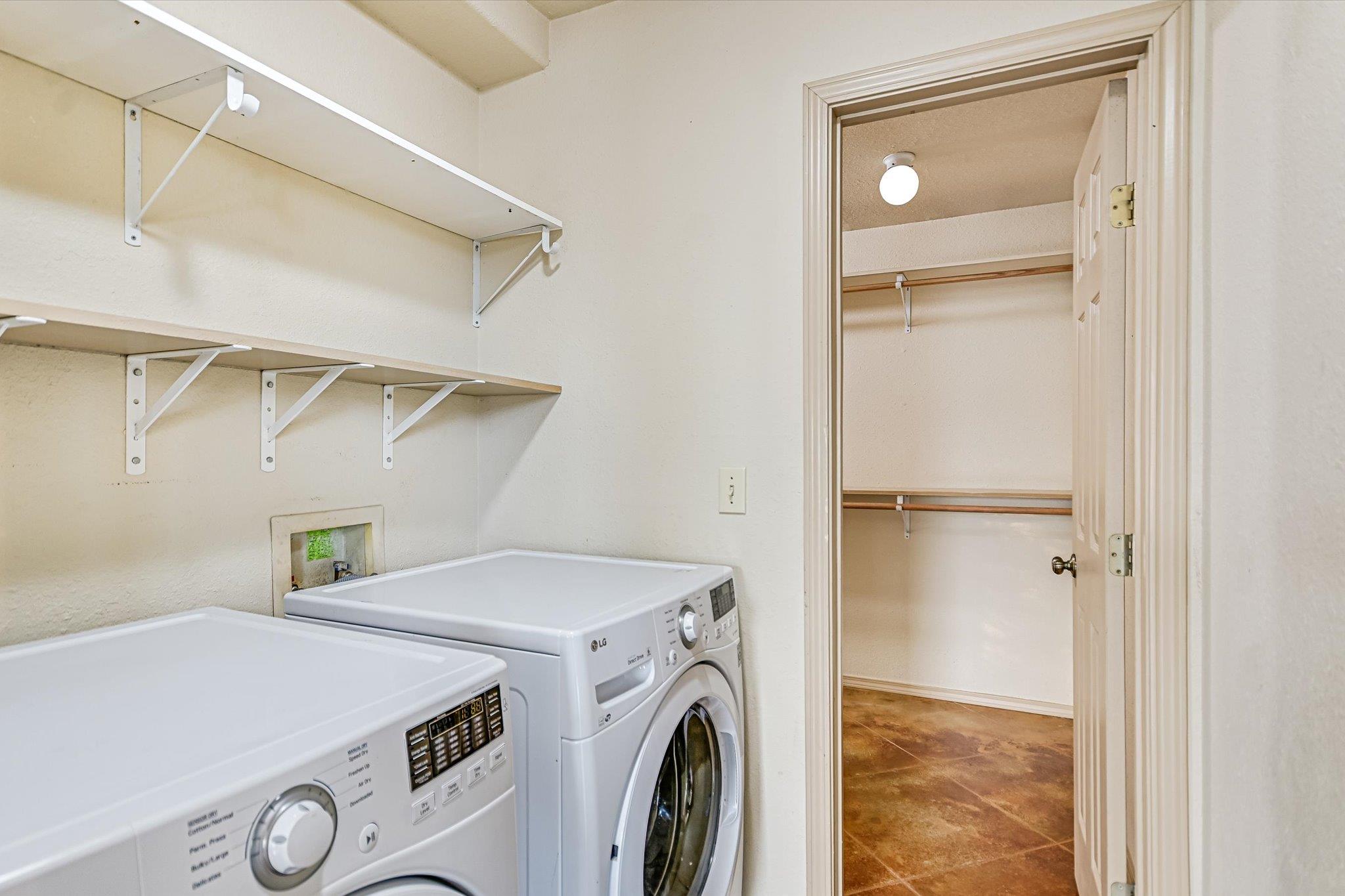 Laundry room with washer and dryer, wall shelves, and an open doorway to a storage closet.