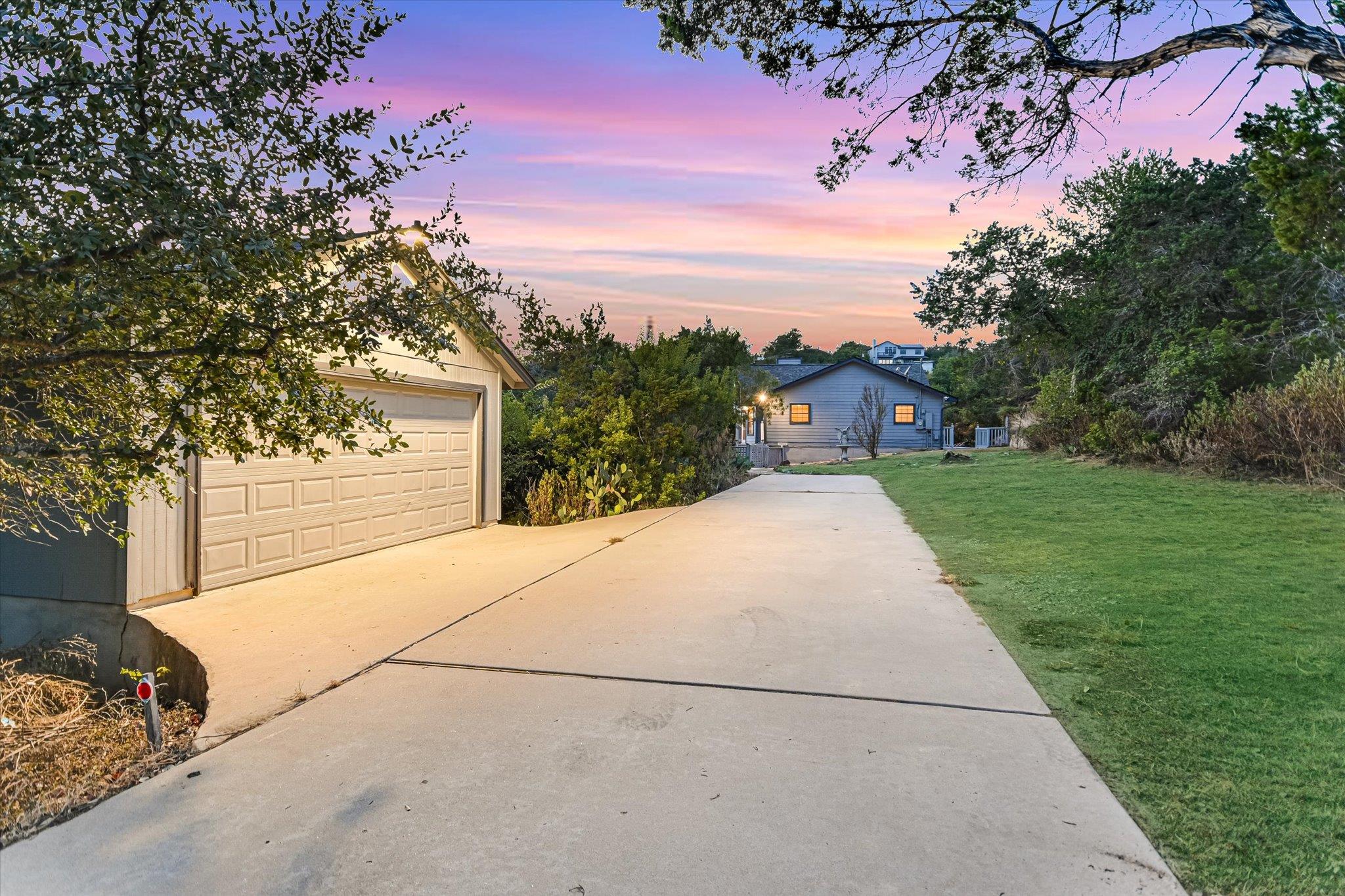 Home exterior at dusk with a long driveway, detached garage, lawn, and mature trees.