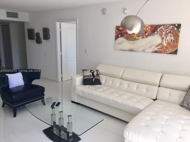 Furnished living room with a white sectional, glass coffee table, and blue armchair.