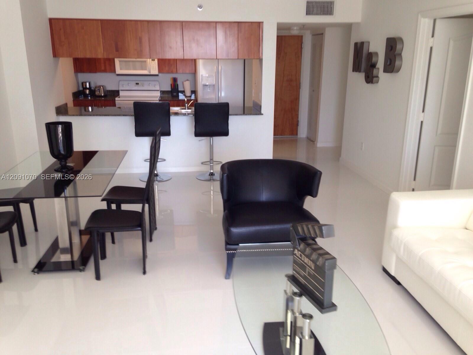 Open-plan living and dining area with a wood-cabinet kitchen, breakfast bar, and black leather chairs.