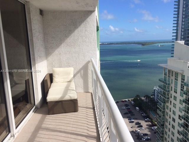 Furnished high-rise balcony overlooking turquoise bay water and neighboring waterfront buildings.