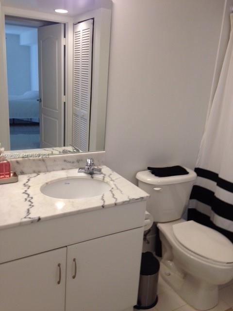 Bathroom with a marble-patterned vanity and mirror beside a toilet and black-and-white shower curtain.