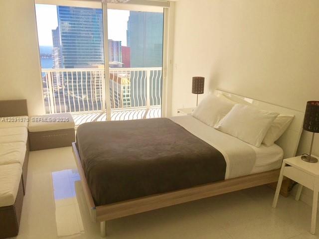 Furnished bedroom with a large bed and balcony overlooking downtown Miami high-rises.