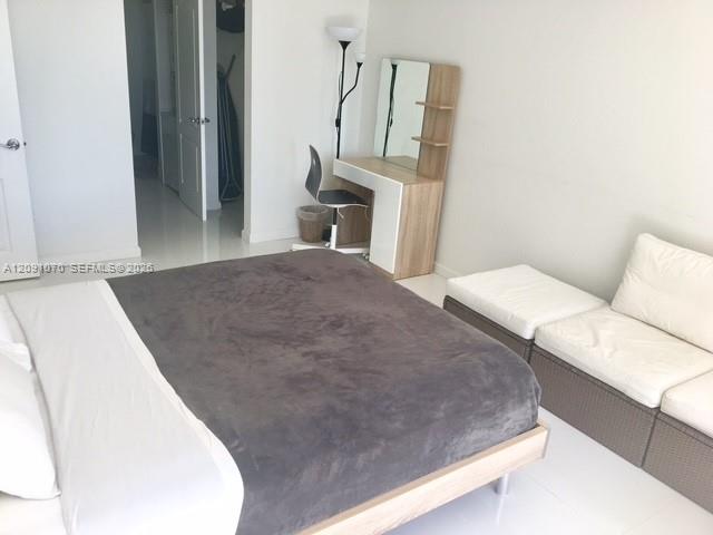 Bedroom with a gray-covered bed, white seating, and a compact vanity.