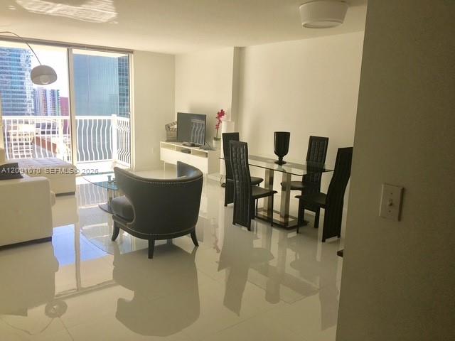Condo living and dining area with a curved armchair, glass dining table, and balcony overlooking the city.