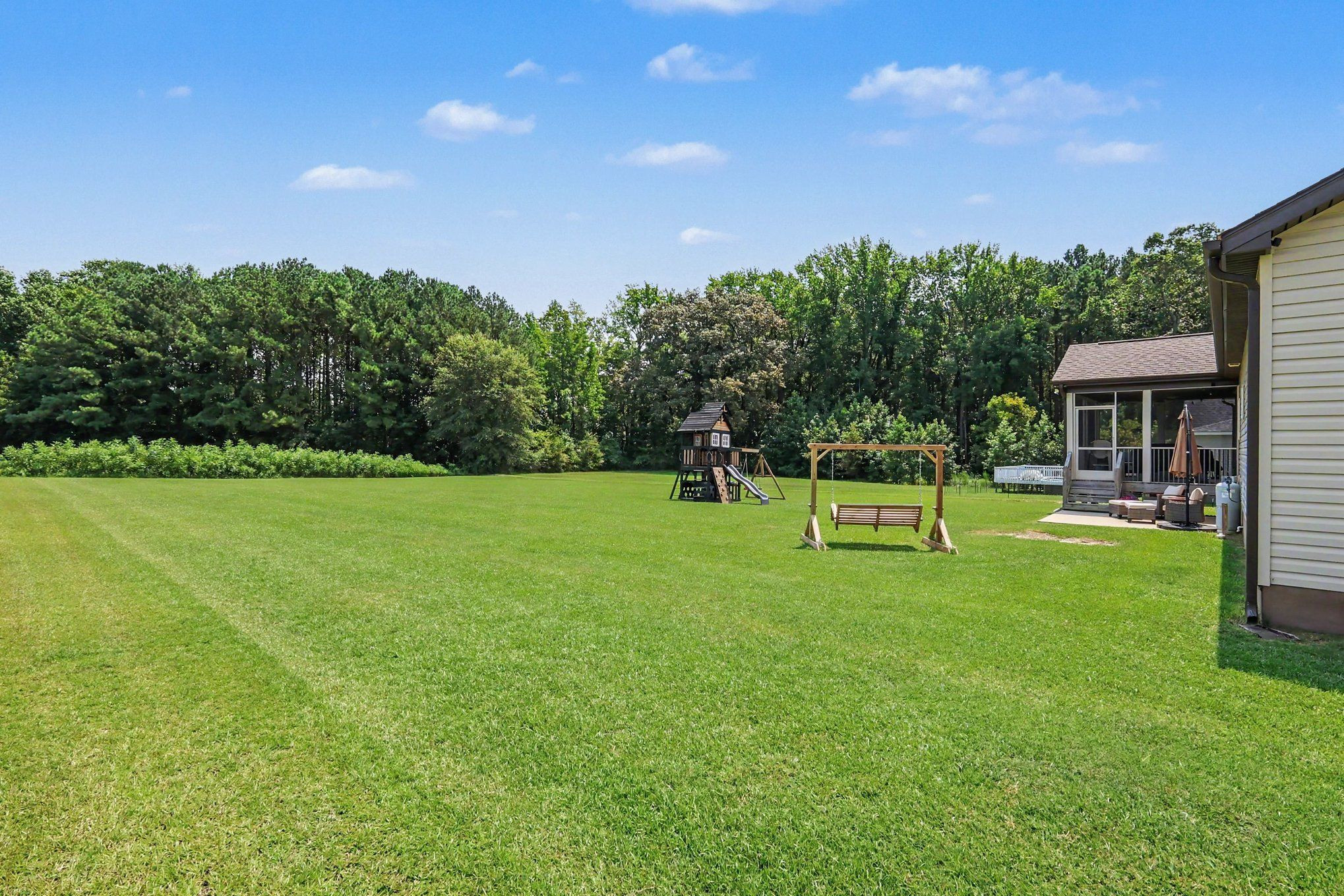 Expansive backyard lawn with a children's playset and swing beside the house.