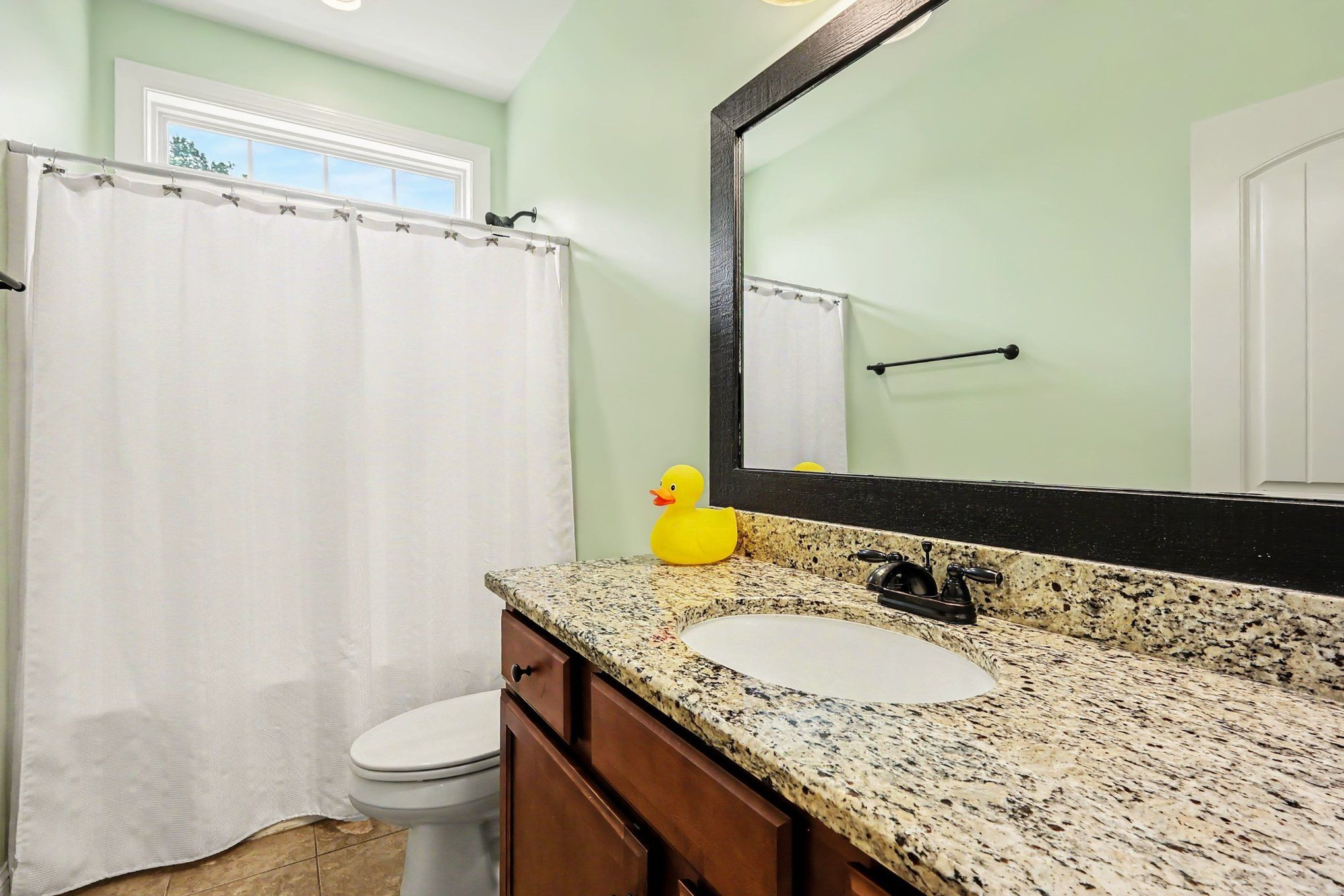 Bathroom vanity with granite countertop, dark wood cabinets, and a yellow rubber duck beside the shower.