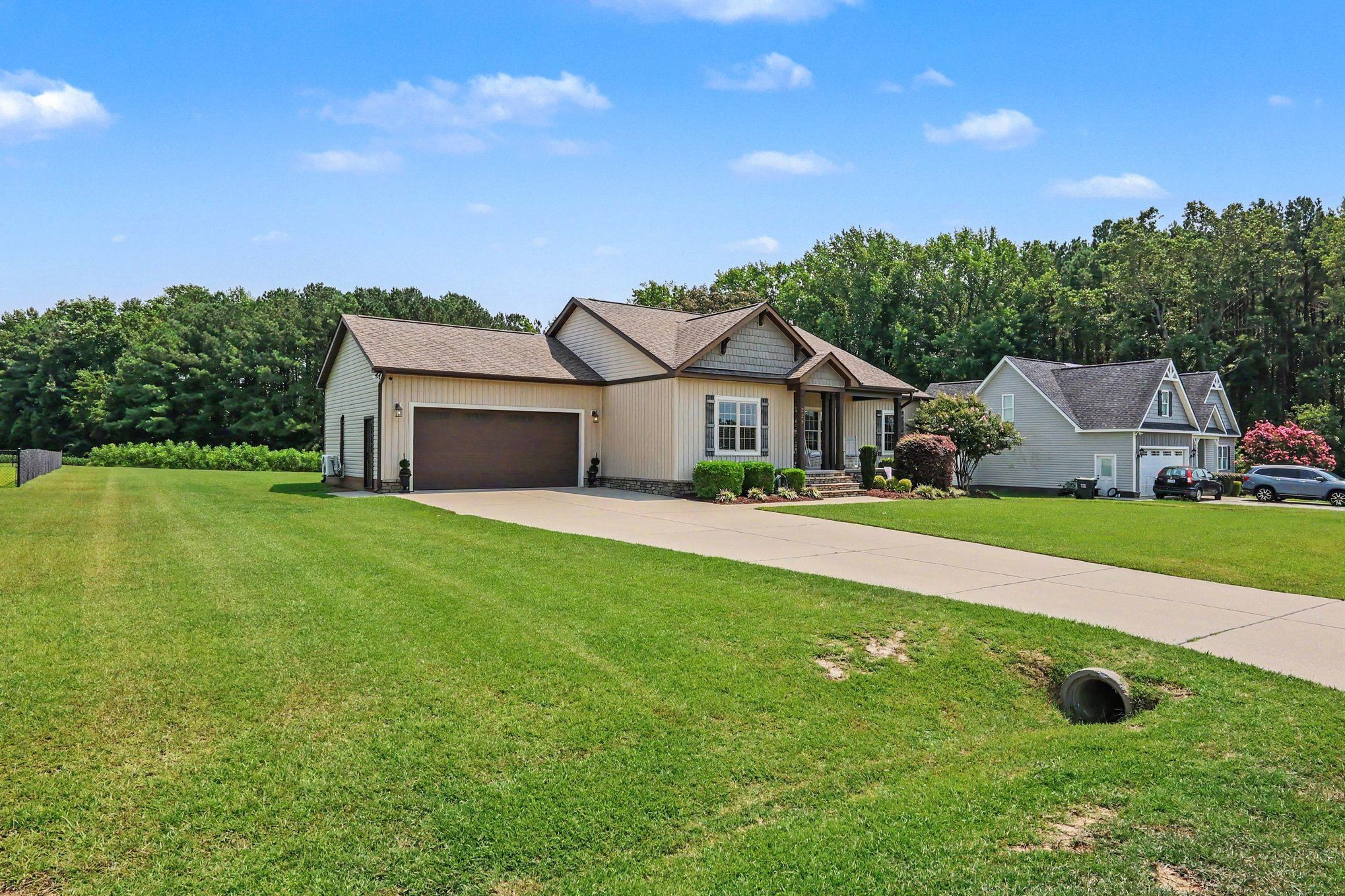 Beige single-story house with a two-car garage, broad lawn, and long concrete driveway.