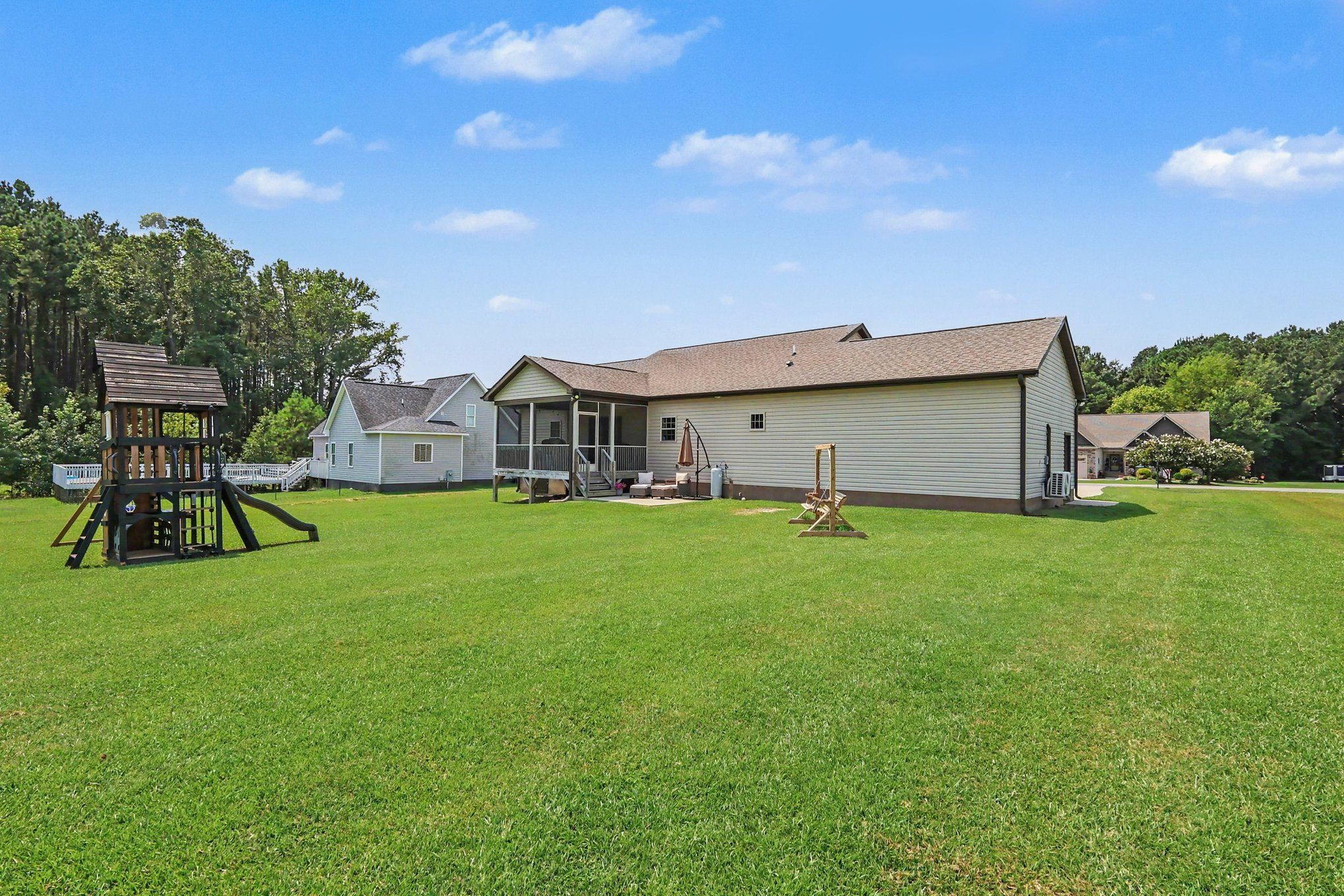 Rear of a single-story home with a screened porch, broad lawn, and wooden playset.