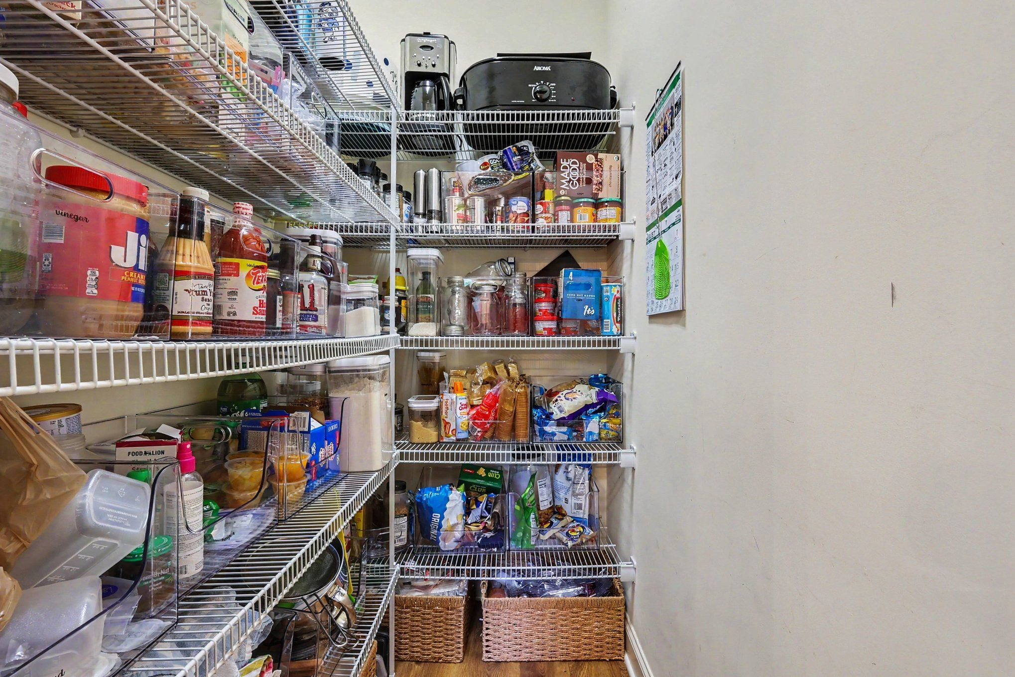 Walk-in pantry with white wire shelves packed with food, jars, appliances, and woven storage baskets.