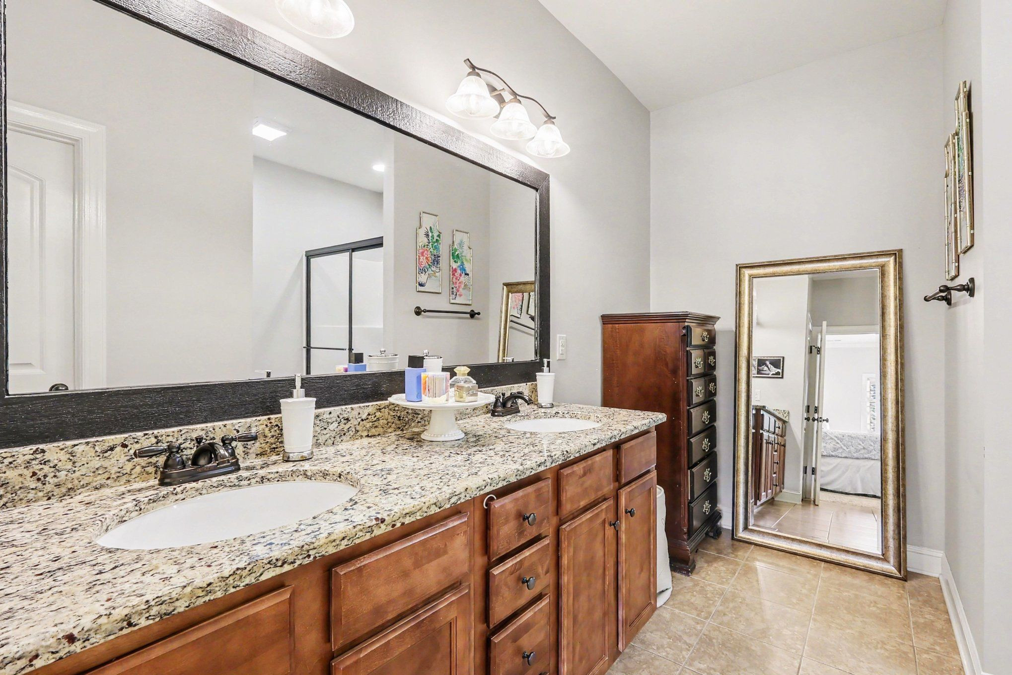 Bathroom with a double-sink granite vanity, wood cabinets, and a full-length mirror.