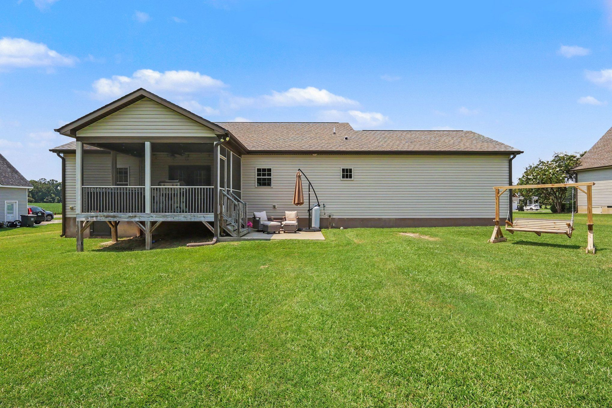 Home’s rear exterior with a screened porch, patio seating, and wooden lawn swing.