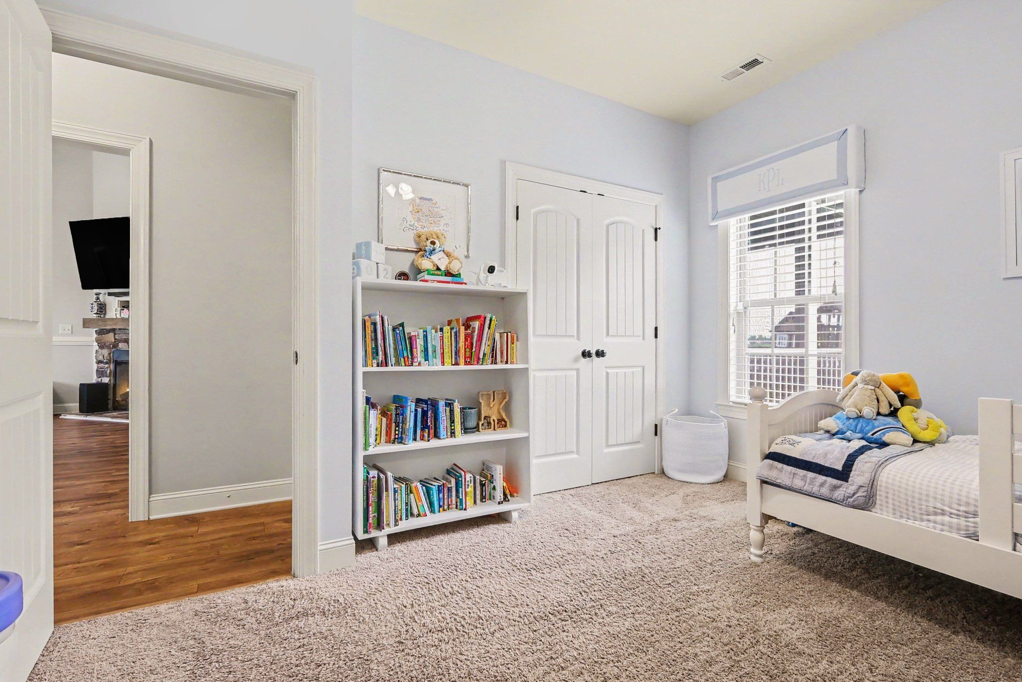 Child's bedroom with a white twin bed, plush toys, and a book-filled shelf beside the closet.
