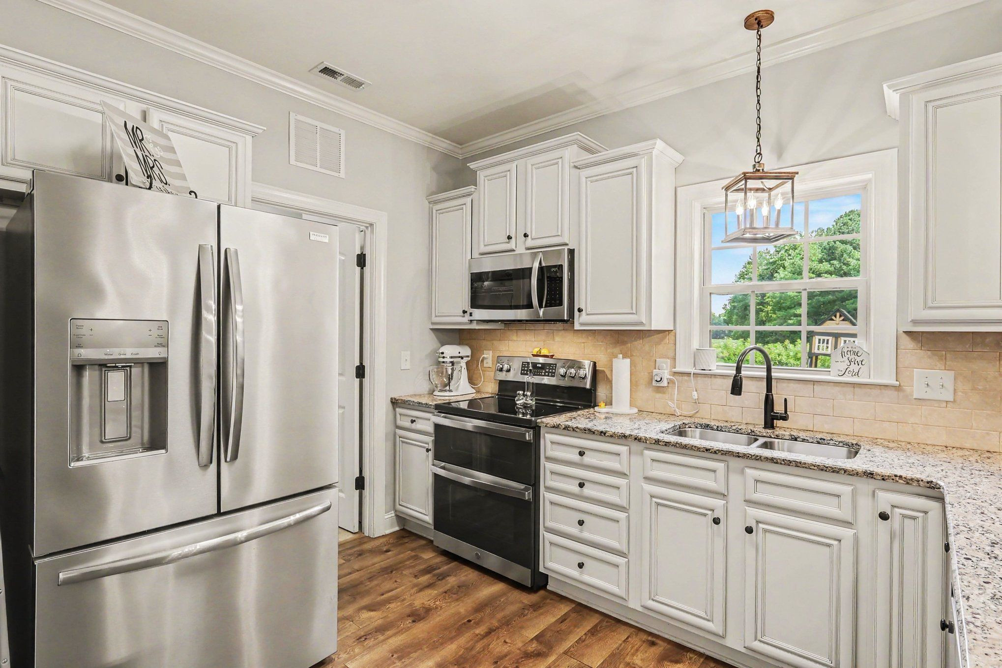 Kitchen with white cabinets, granite counters, stainless steel appliances, and a window over the sink.