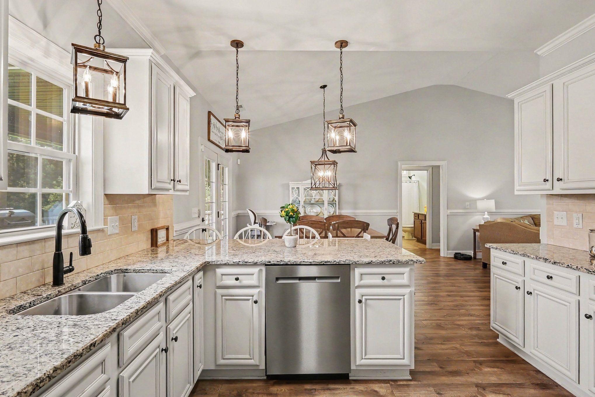 Kitchen with white cabinets, granite counters, a central island, and a dining area beyond.