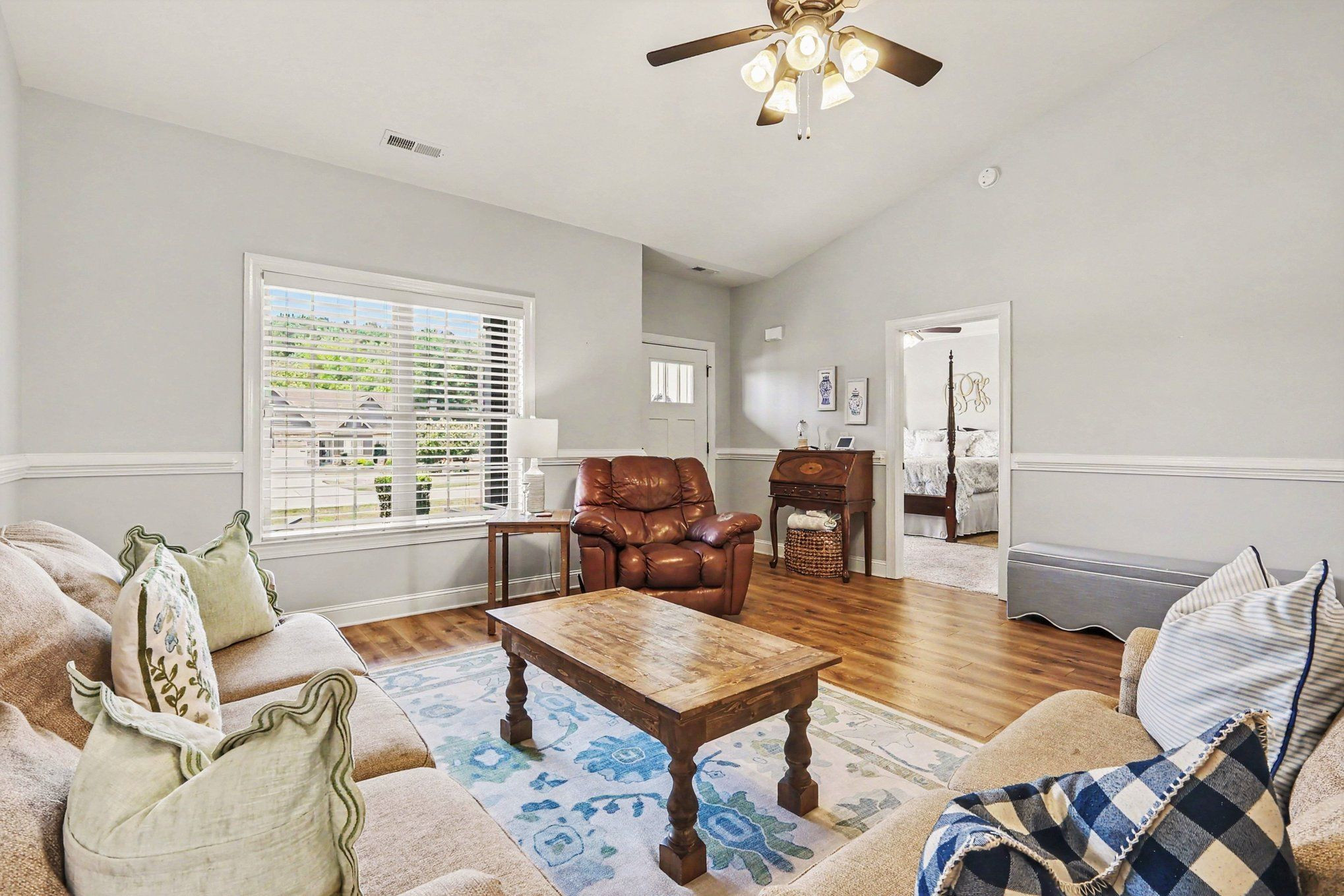Living room with a large window, wood floors, sofas, and a brown leather recliner.