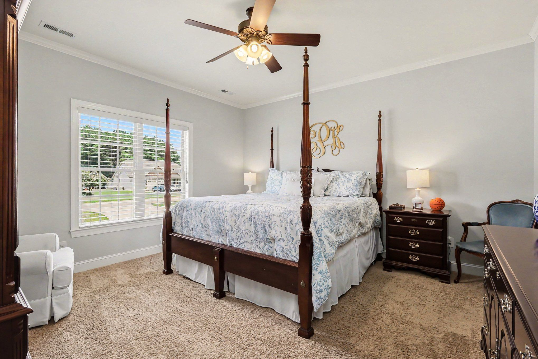 Bedroom with a dark wood four-poster bed, blue floral bedding, and a large window with white blinds.