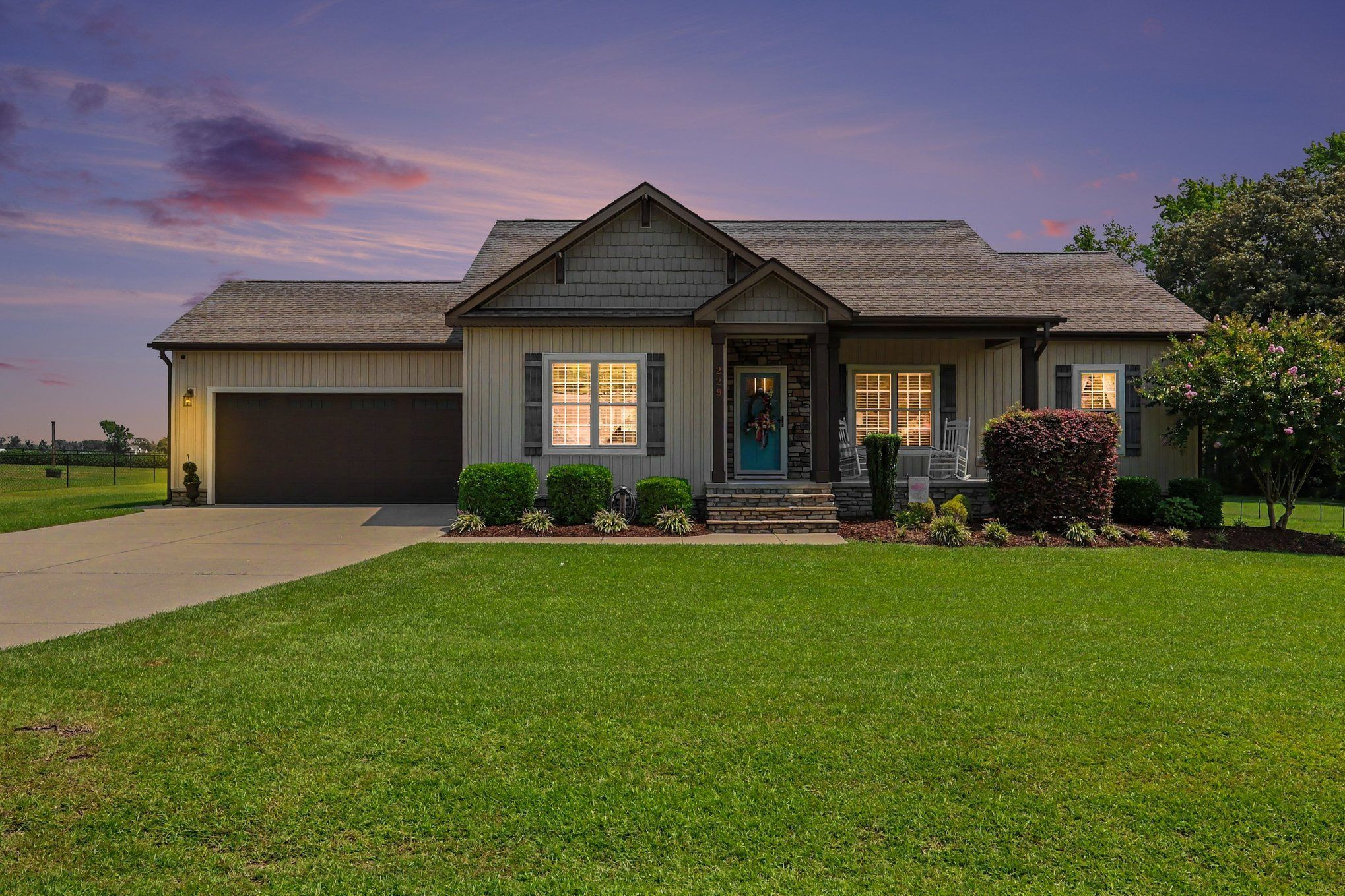 Gray single-story home at dusk with a stone-accented porch, two-car garage, and broad green lawn.
