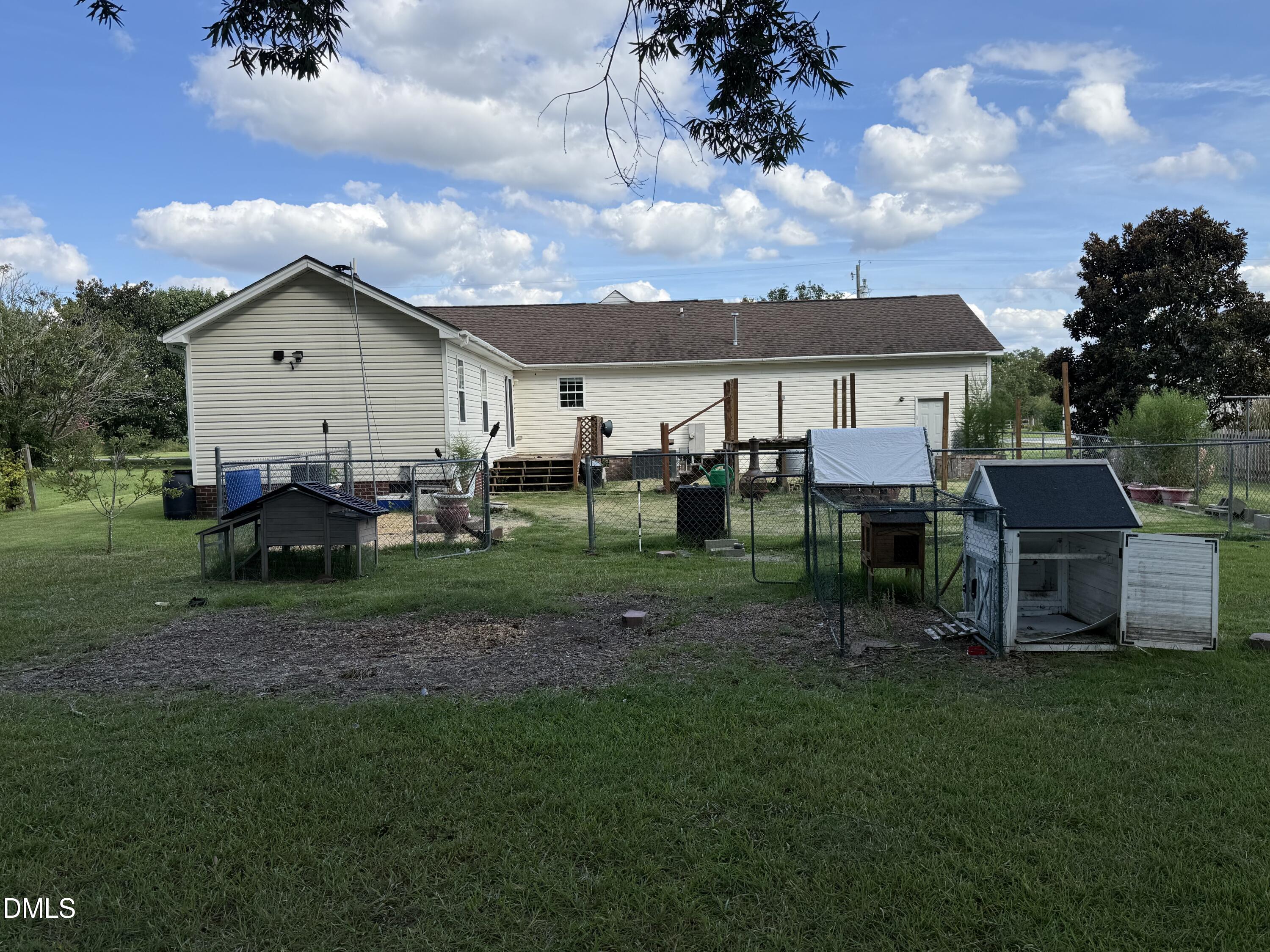 Rear of a white-sided home with a fenced grassy yard and several animal hutches.