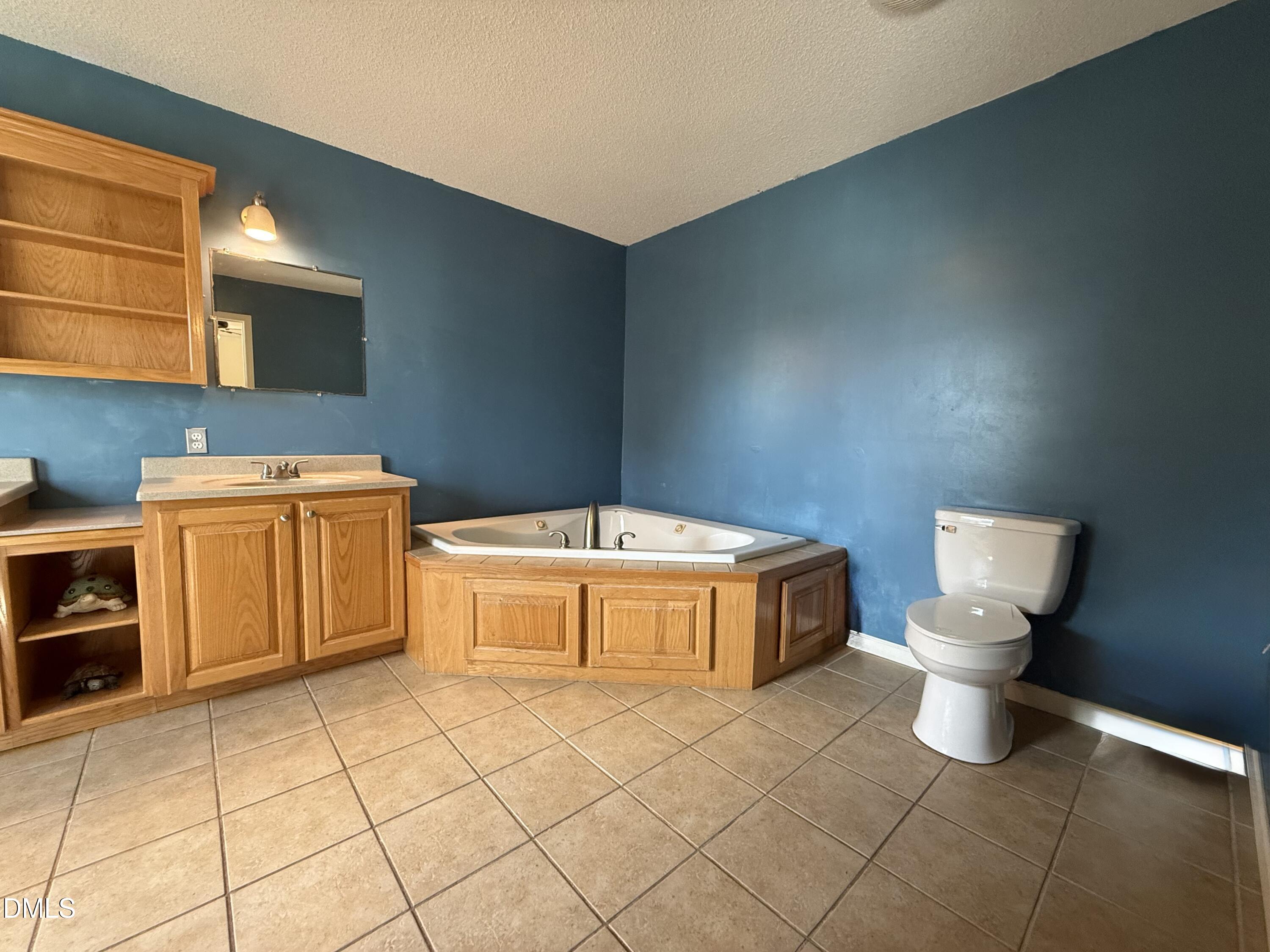 Bathroom with a corner jetted tub, oak cabinetry, blue walls, and tan tile flooring.