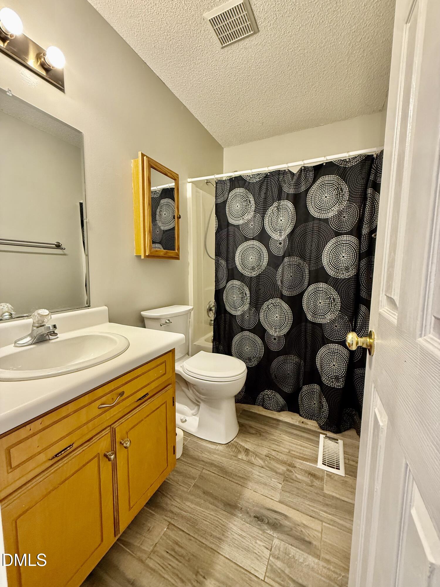 Bathroom with a honey-colored vanity, white fixtures, and a black-and-white circular shower curtain.