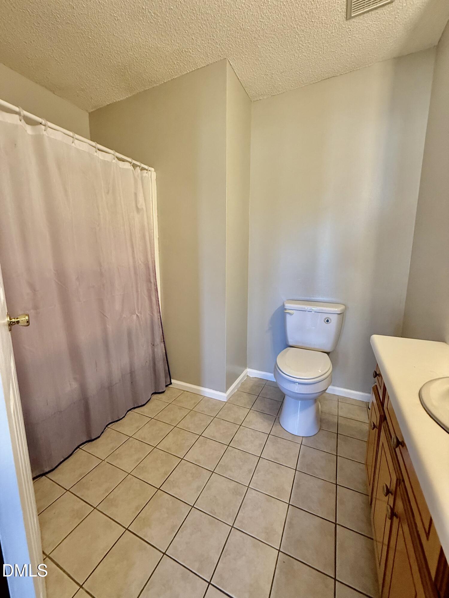 Bathroom with a mauve shower curtain, tiled floor, white toilet, and wood vanity.