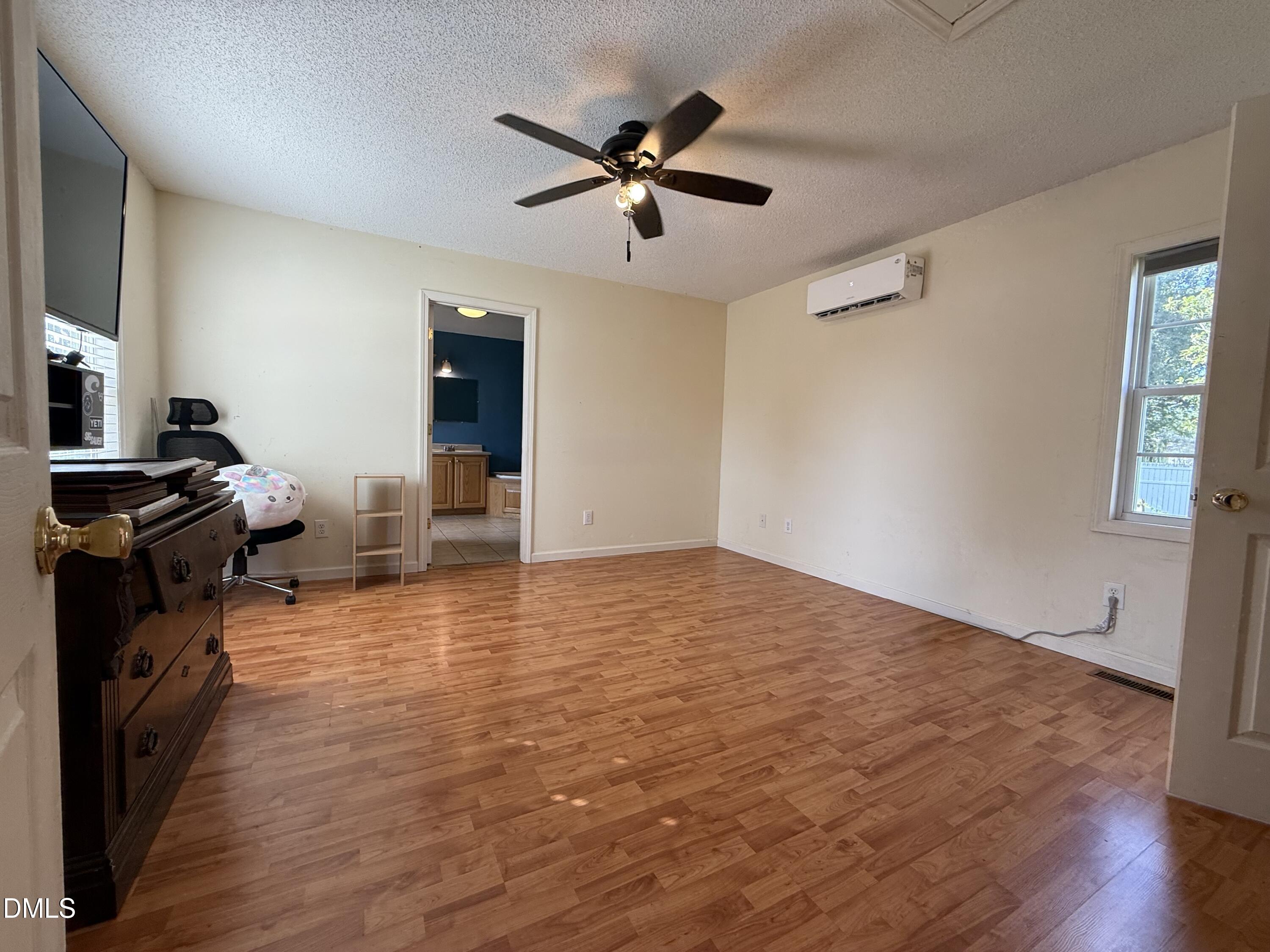 Bedroom with wood-look flooring, ceiling fan, and wall-mounted mini-split air conditioner.