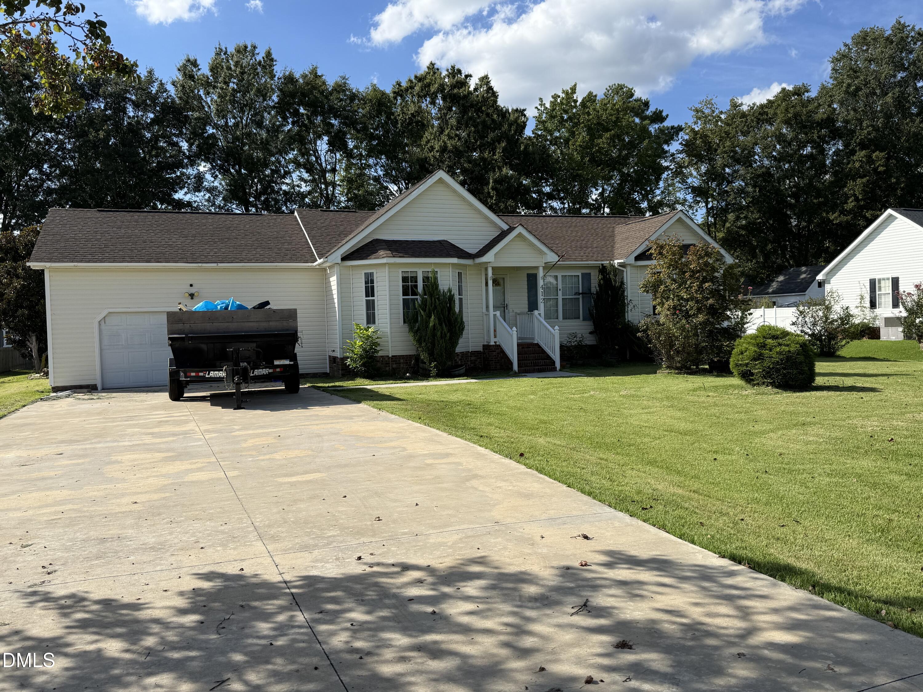 Single-story white home with a garage, small porch, and black trailer in the driveway.