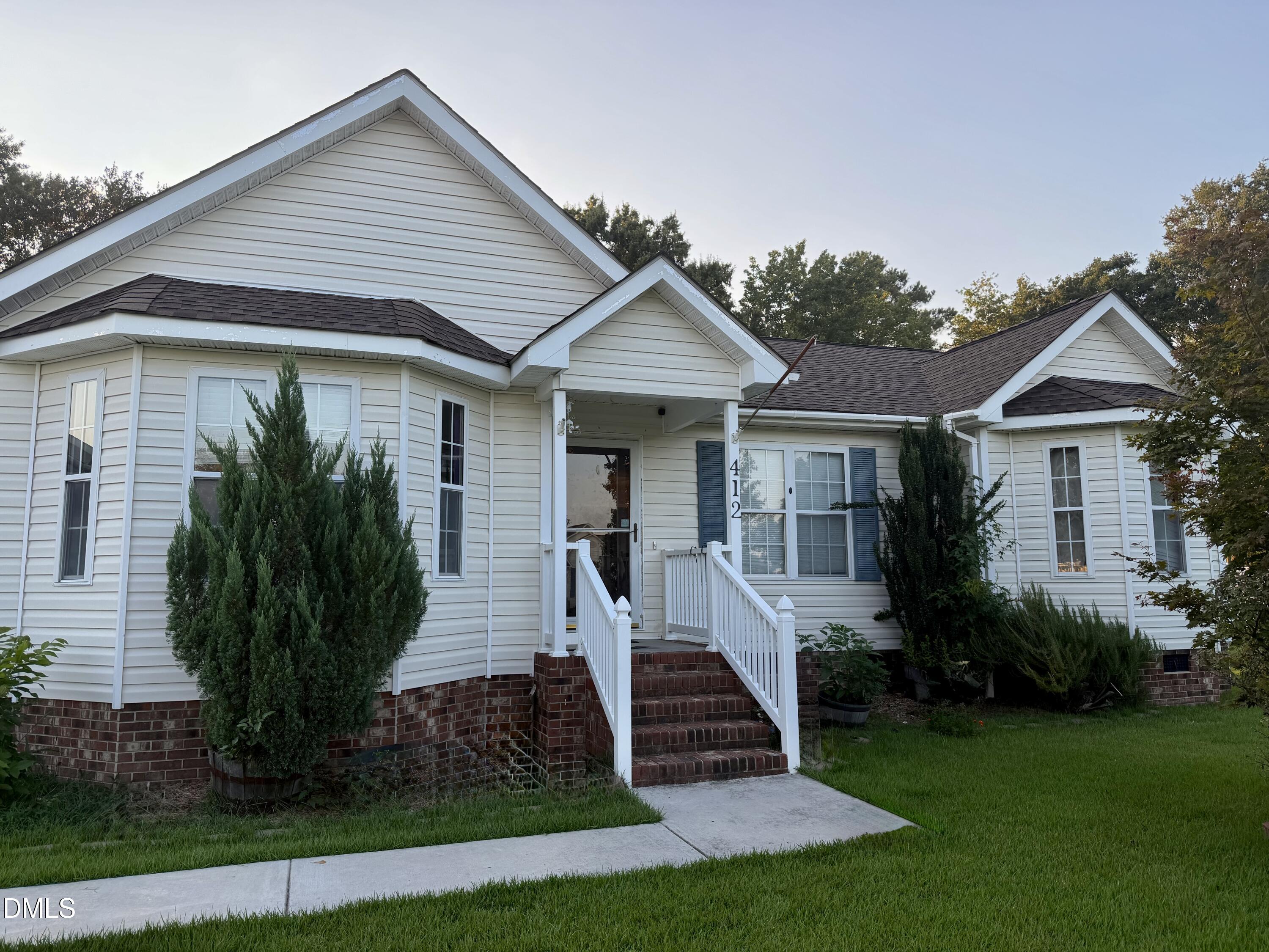 White-sided home with brick steps, a covered entry, and shrubs along the front.