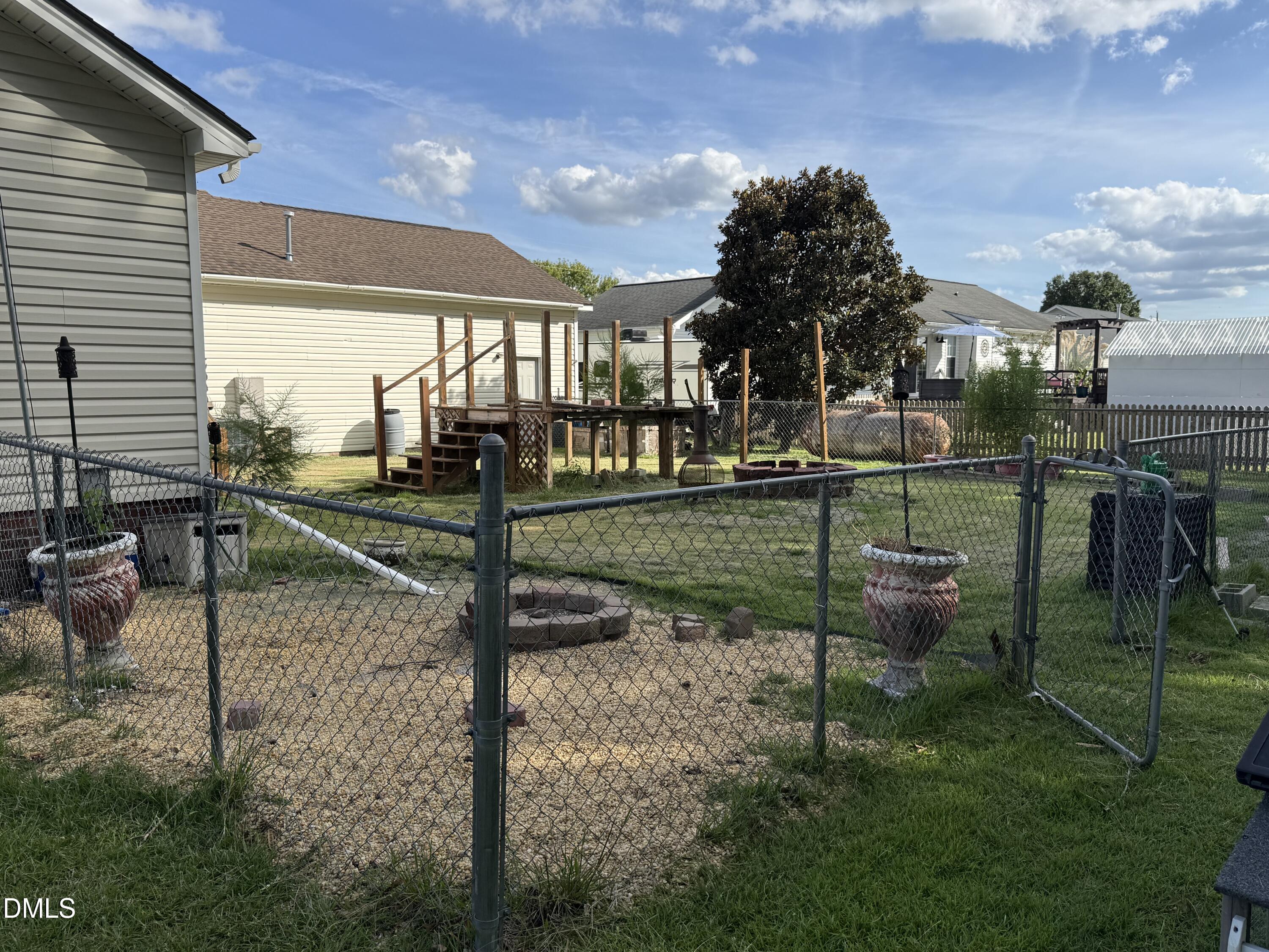 Fenced backyard with a raised wooden deck, gravel area, lawn, and mature tree.