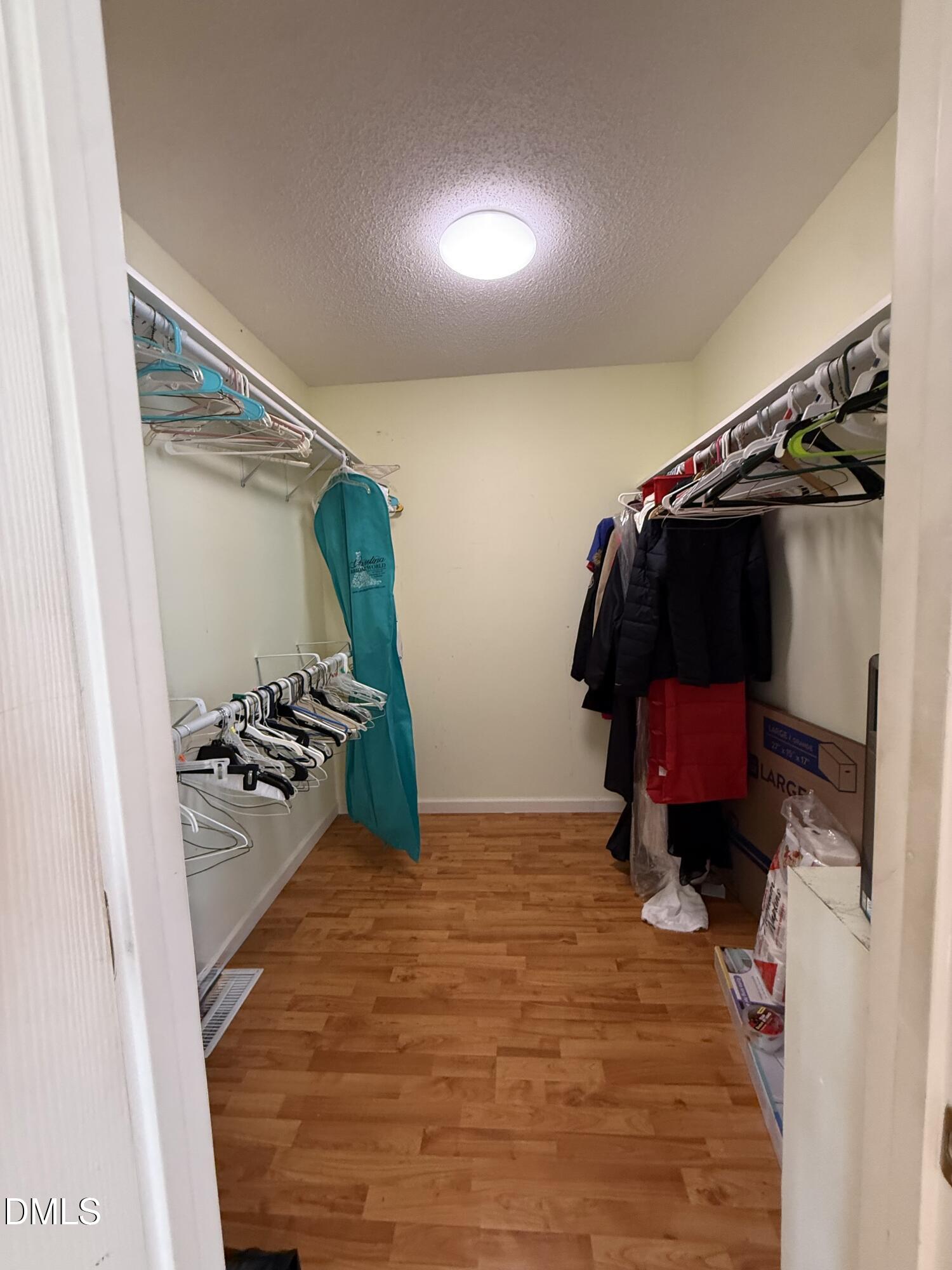 Walk-in closet with hanging clothes, wood-look flooring, and storage boxes.
