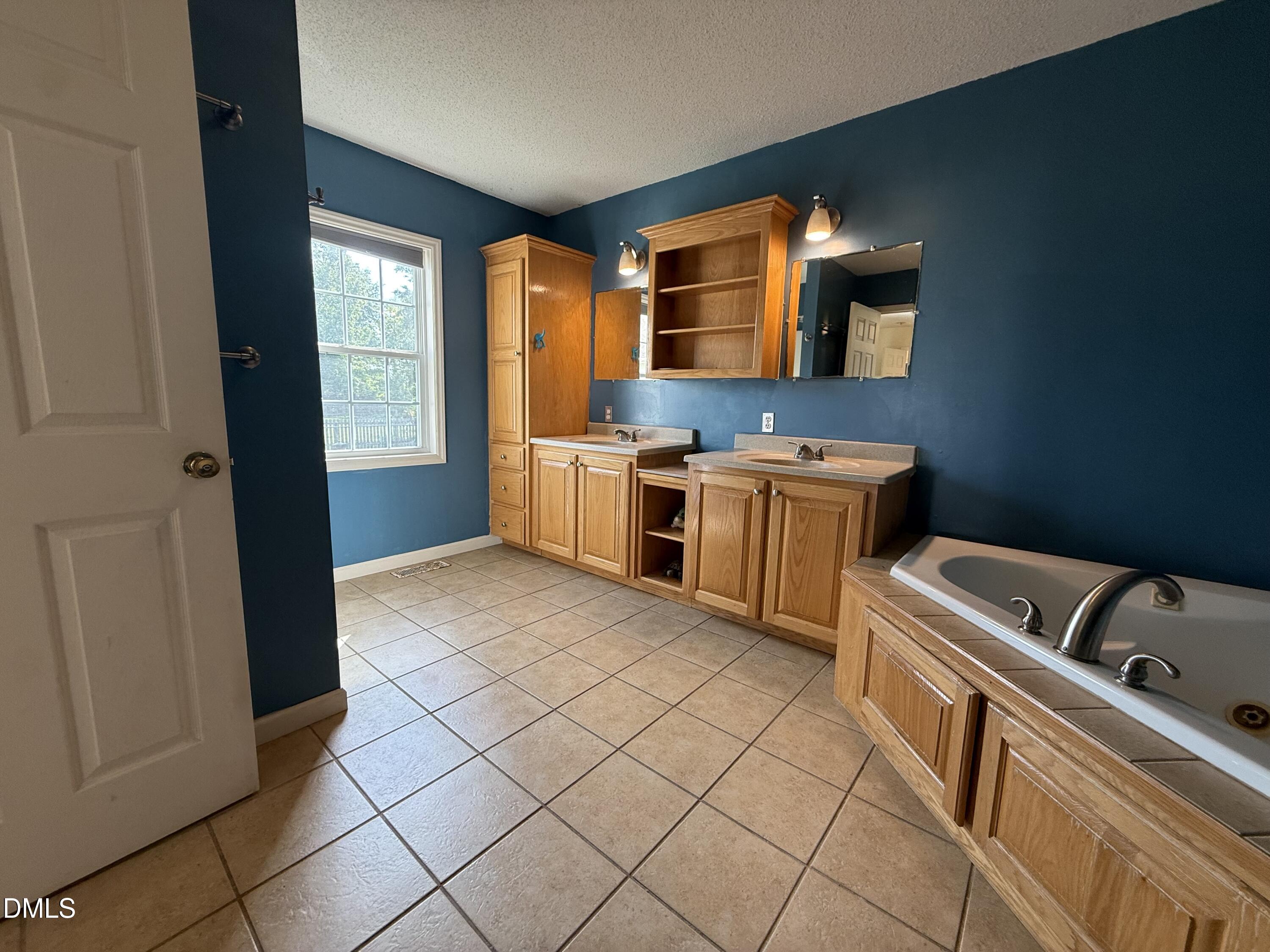 Bathroom with blue walls, wood double vanity, mirrored cabinets, and built-in bathtub.