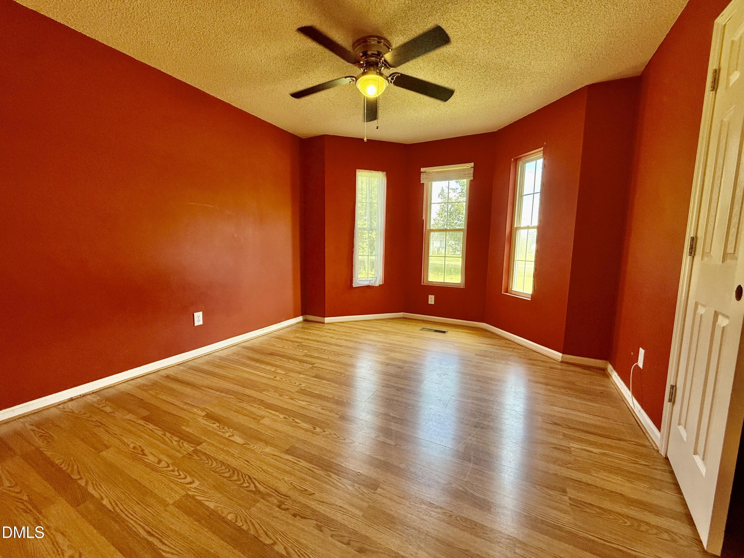 Empty red bedroom with wood-look flooring, three windows, and a ceiling fan.