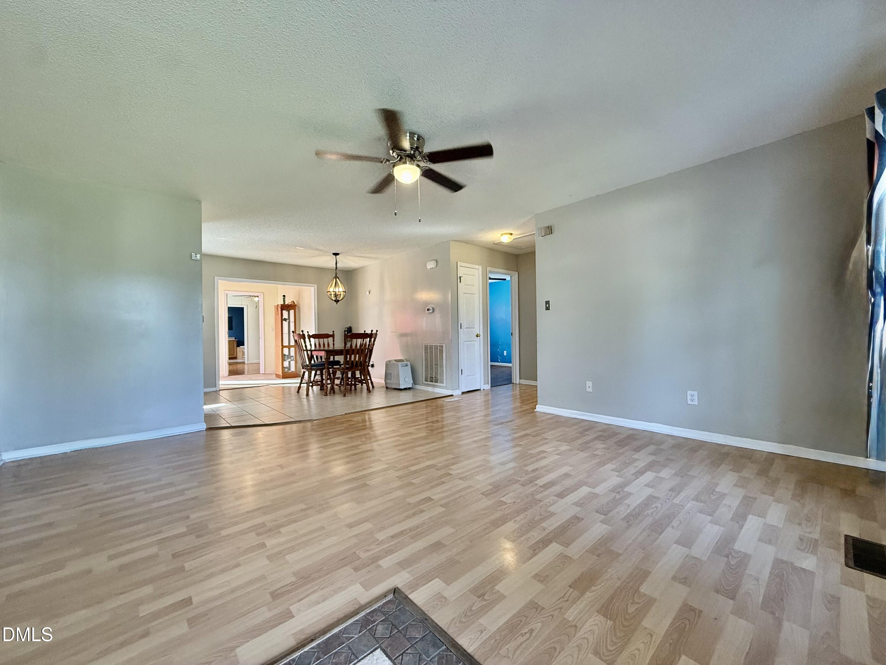 Living room with light wood flooring and ceiling fan, opening to a tiled dining area.