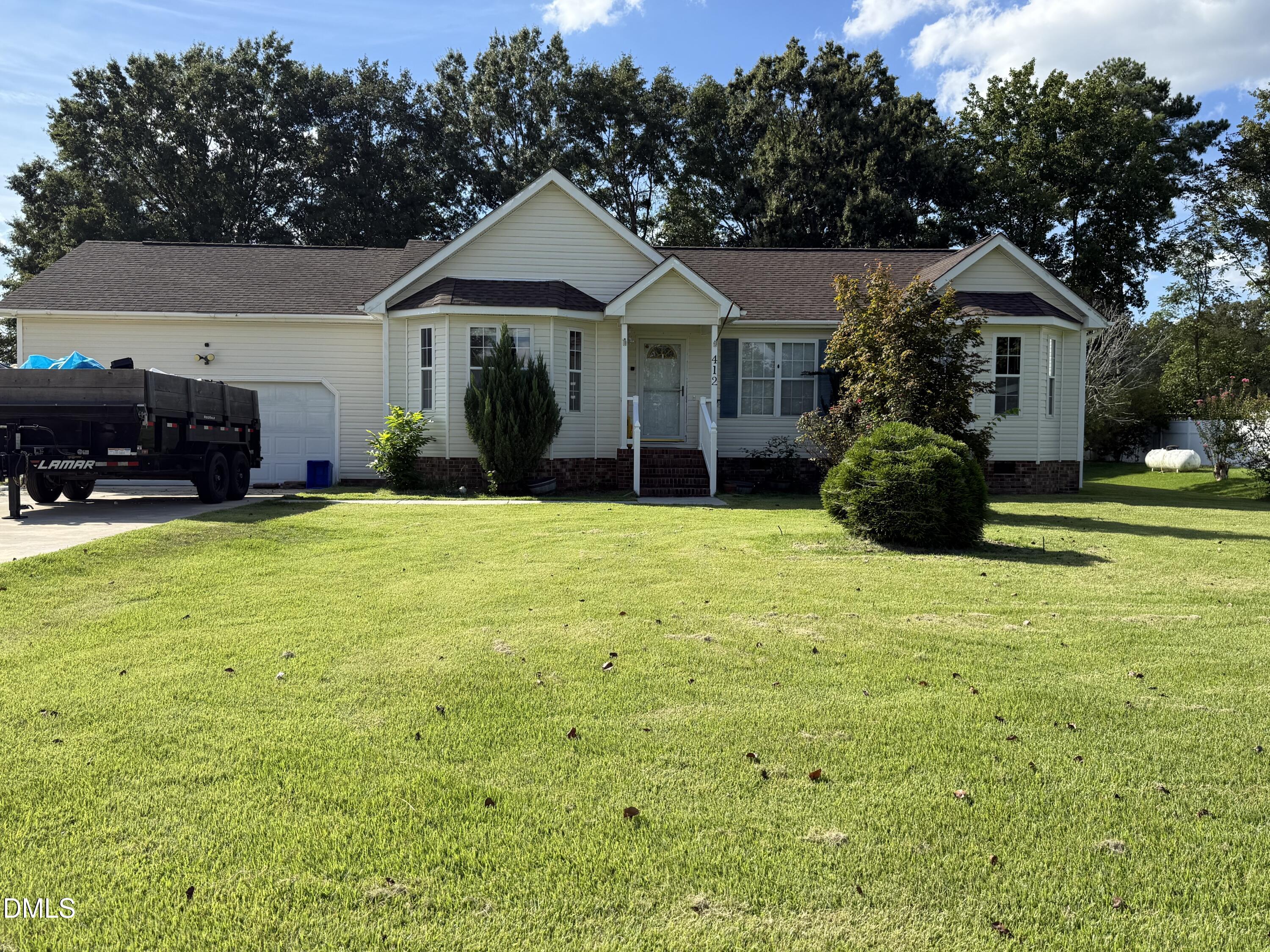 Single-story house with a broad lawn, attached garage, and black dump trailer in the driveway.