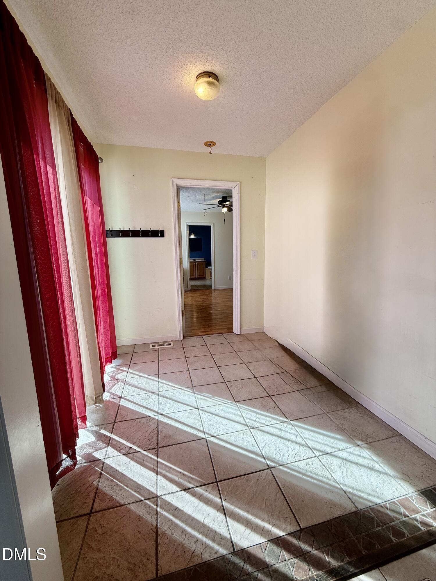 Tiled entry hallway with red curtains and sunlight stretching across the floor.