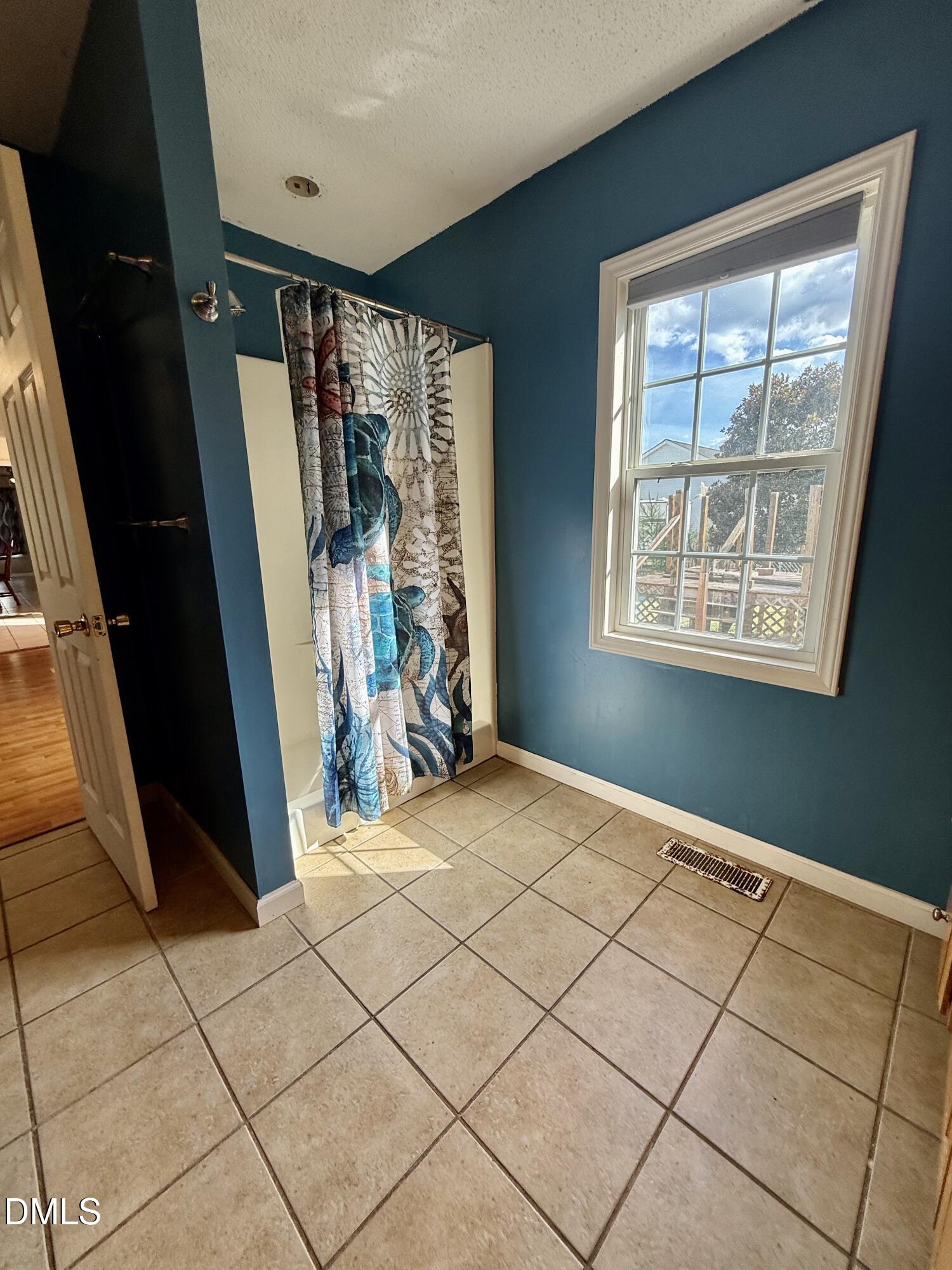 Bathroom with teal walls, tiled floor, patterned shower curtain, and a sunlit window.