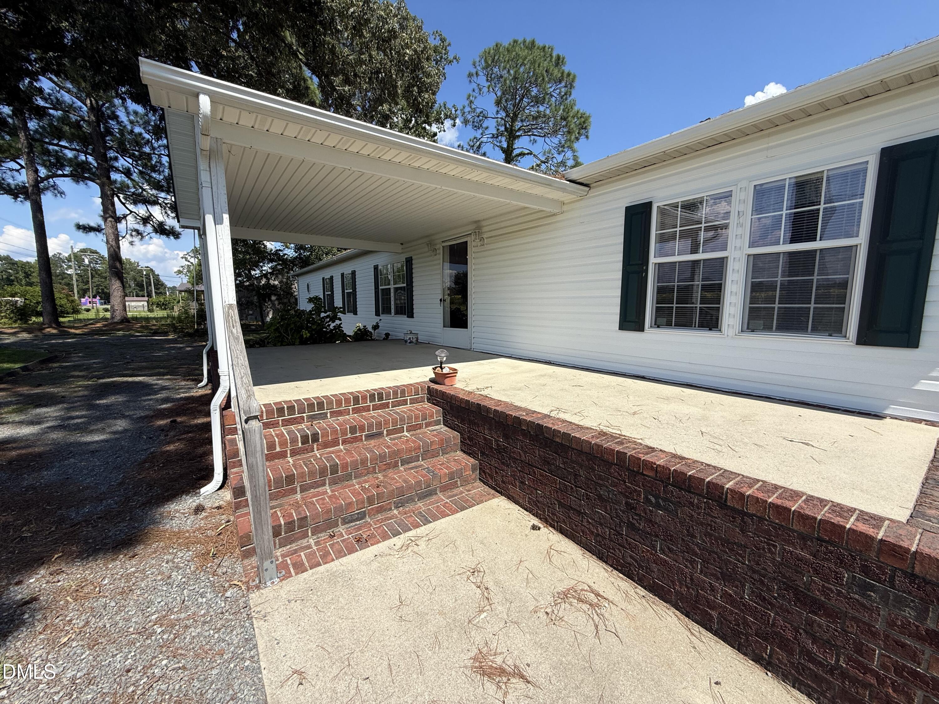 Covered patio with brick steps beside a white-sided home with dark green shutters.