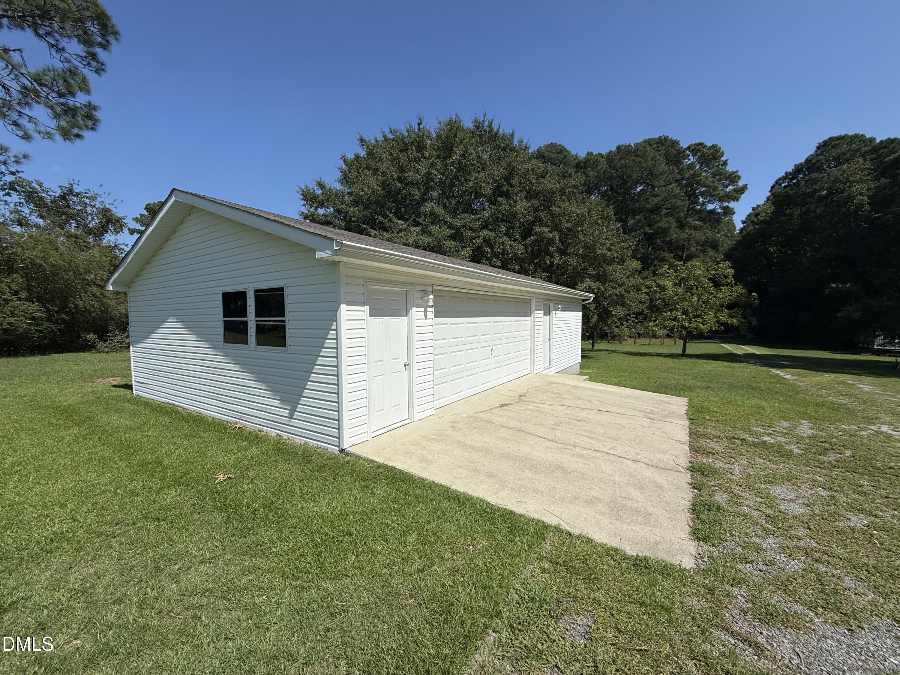 White detached garage with multiple doors and a concrete driveway beside a grassy yard.