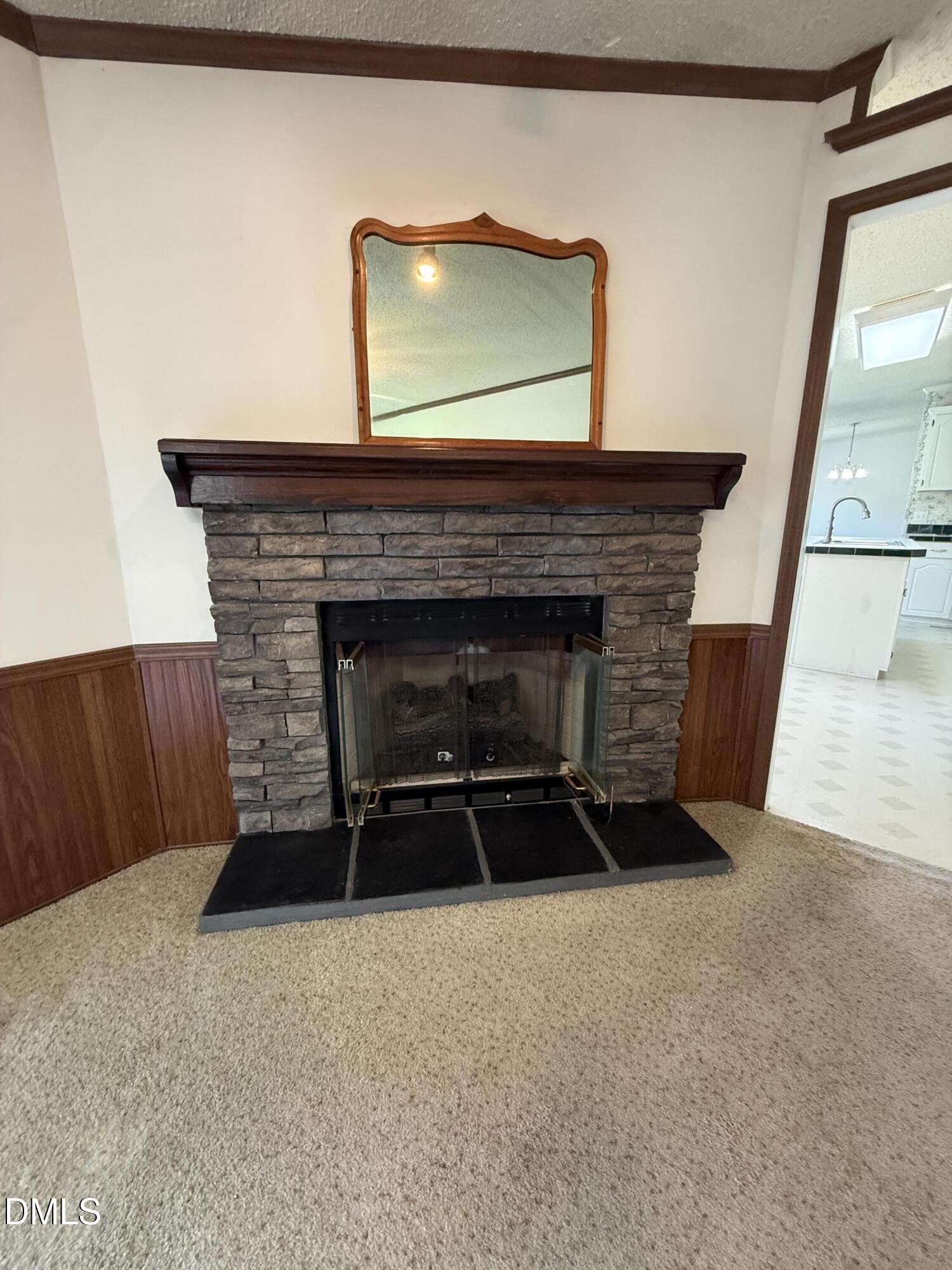 Stone fireplace with glass doors and a dark wood mantel beneath a framed mirror.