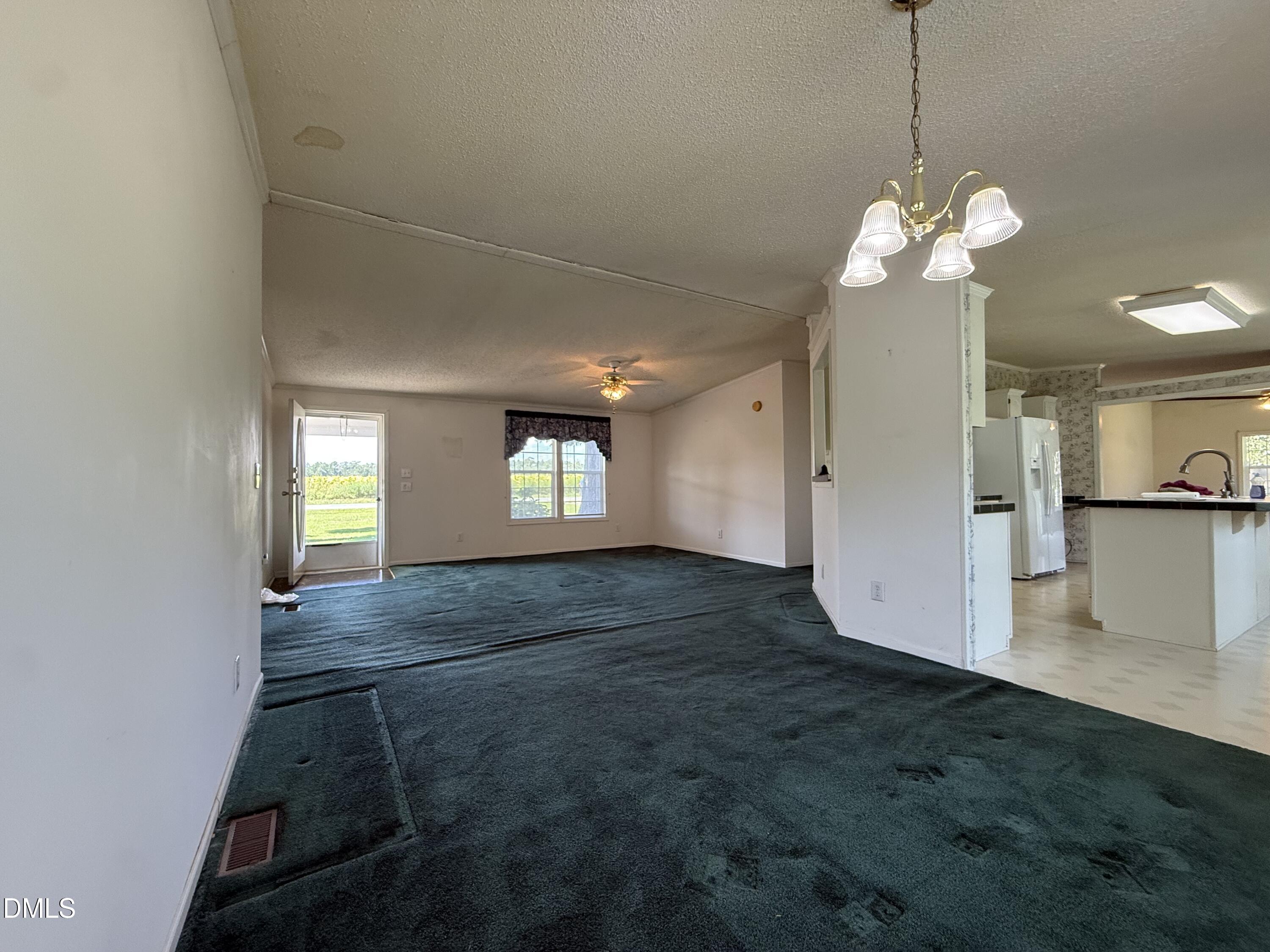 Unfurnished living area with dark teal carpet, a chandelier, and an open door to the lawn.