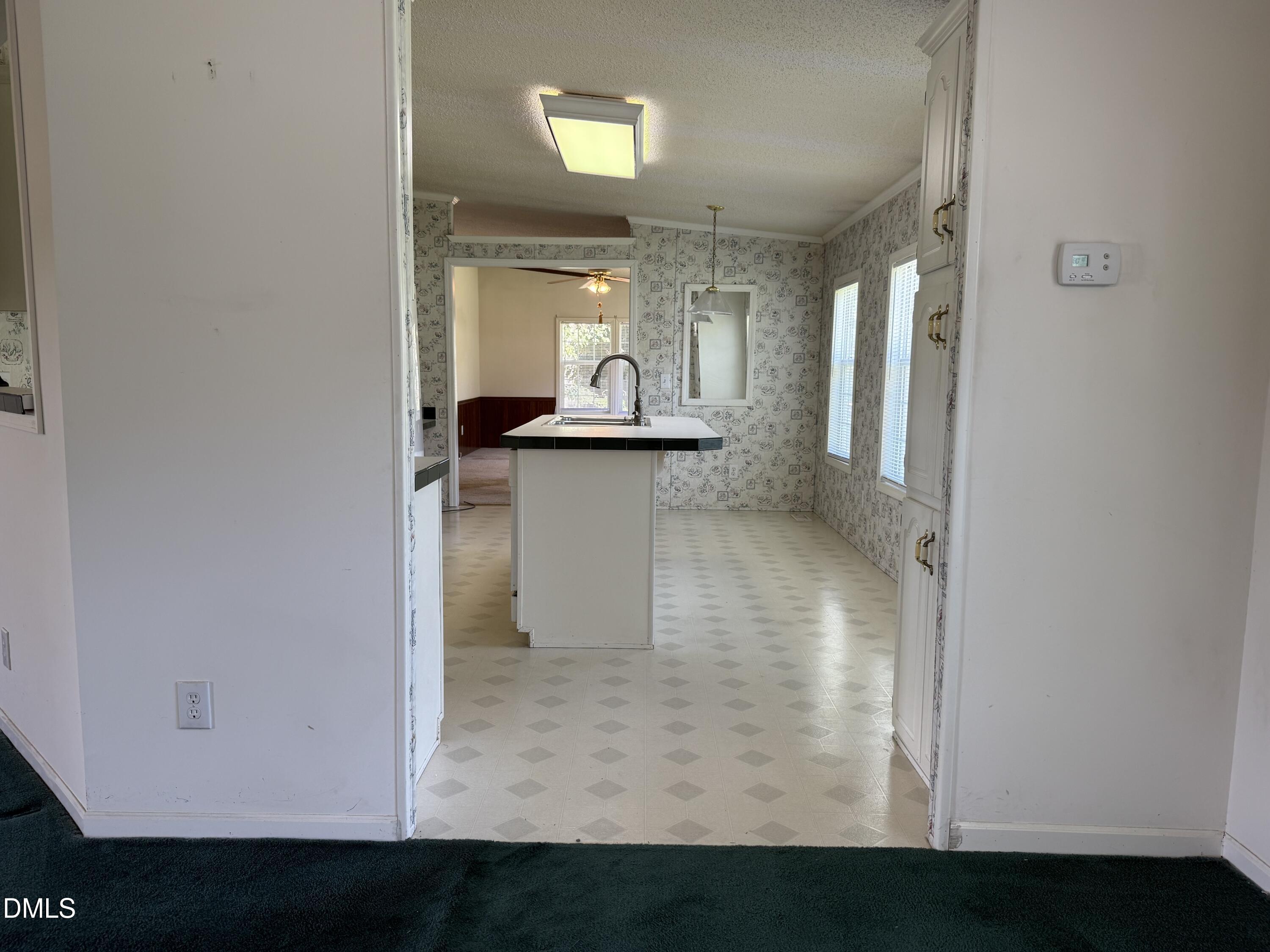 Empty kitchen with a central sink island, patterned wallpaper, and diamond-pattern flooring.