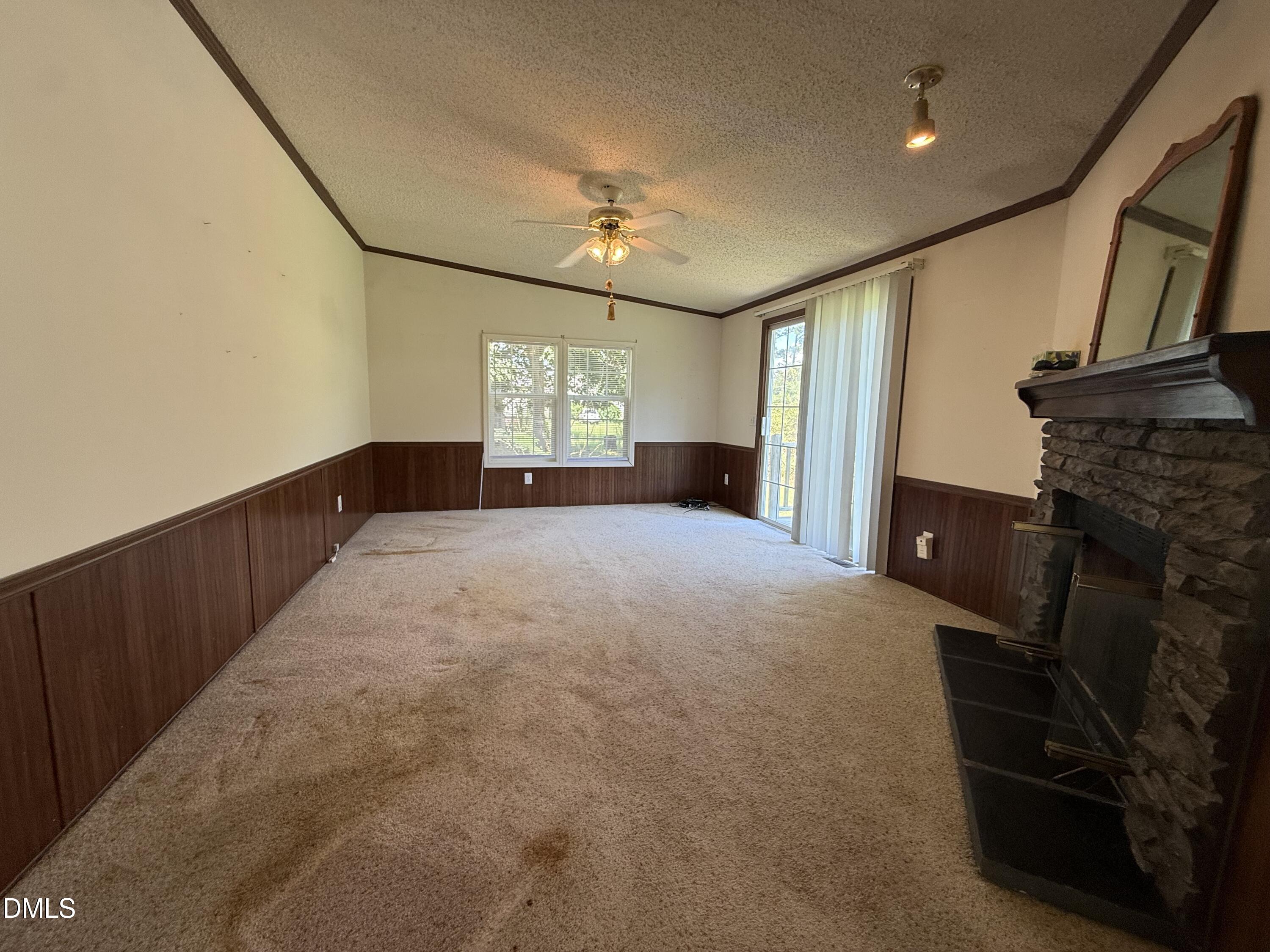 Empty living room with stained carpet, dark wood paneling, and a stone fireplace.