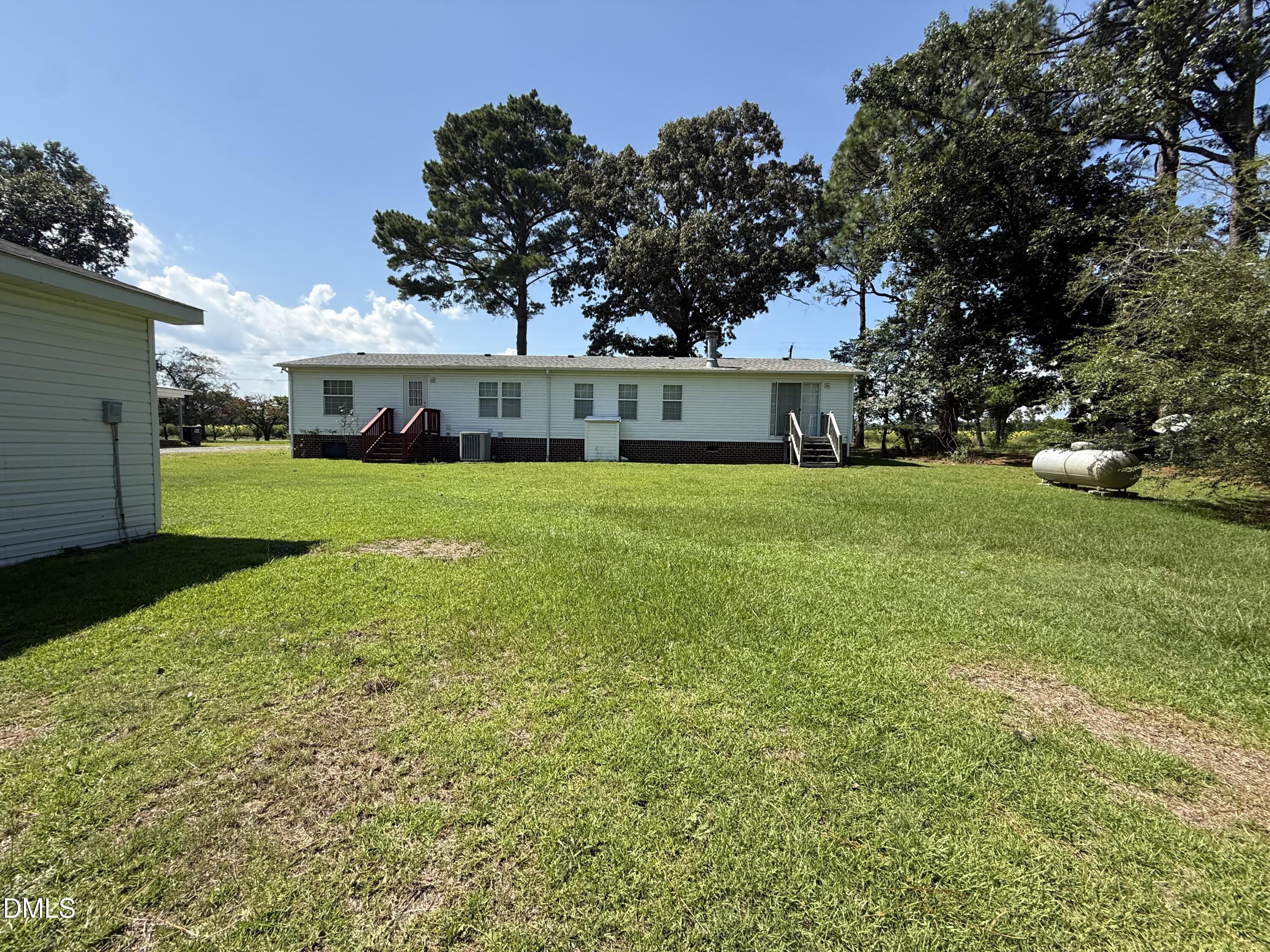 Rear of a single-story home with a broad lawn, mature trees, and a propane tank.