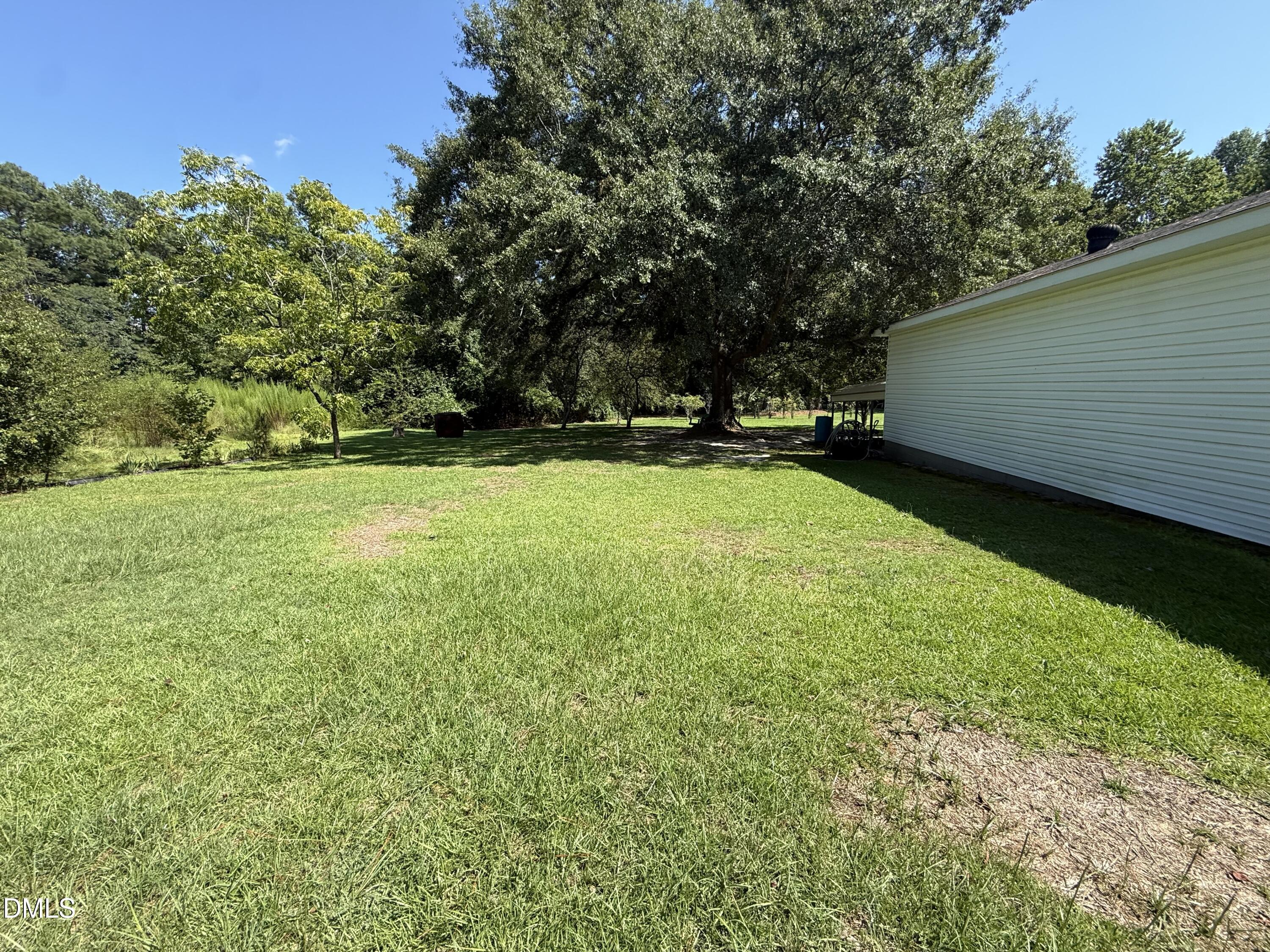 Grassy backyard beside a white-sided home, shaded by mature trees.