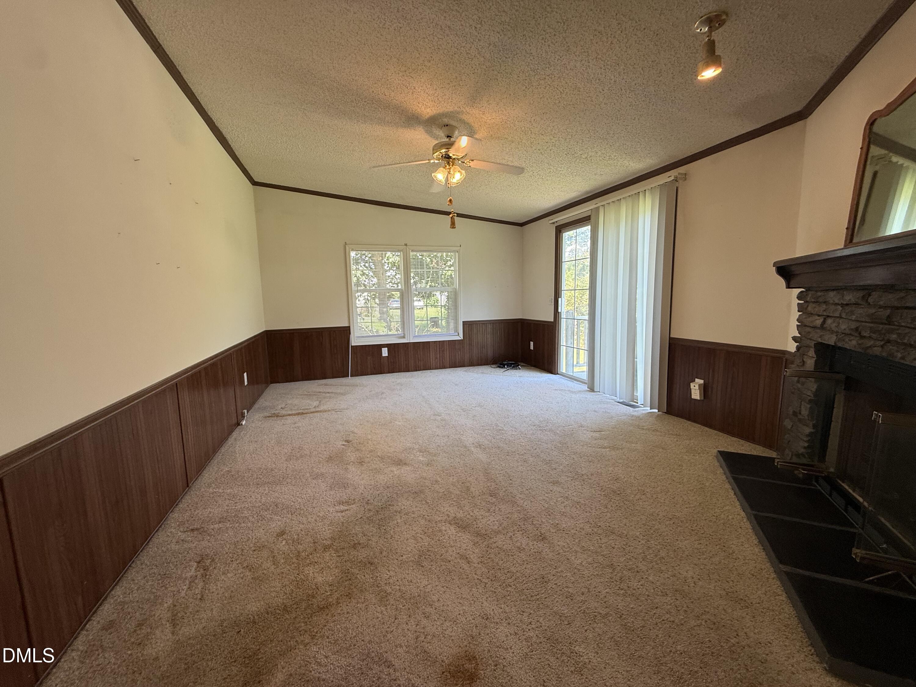 Empty living room with a stone fireplace, wood-paneled walls, and sliding glass door.