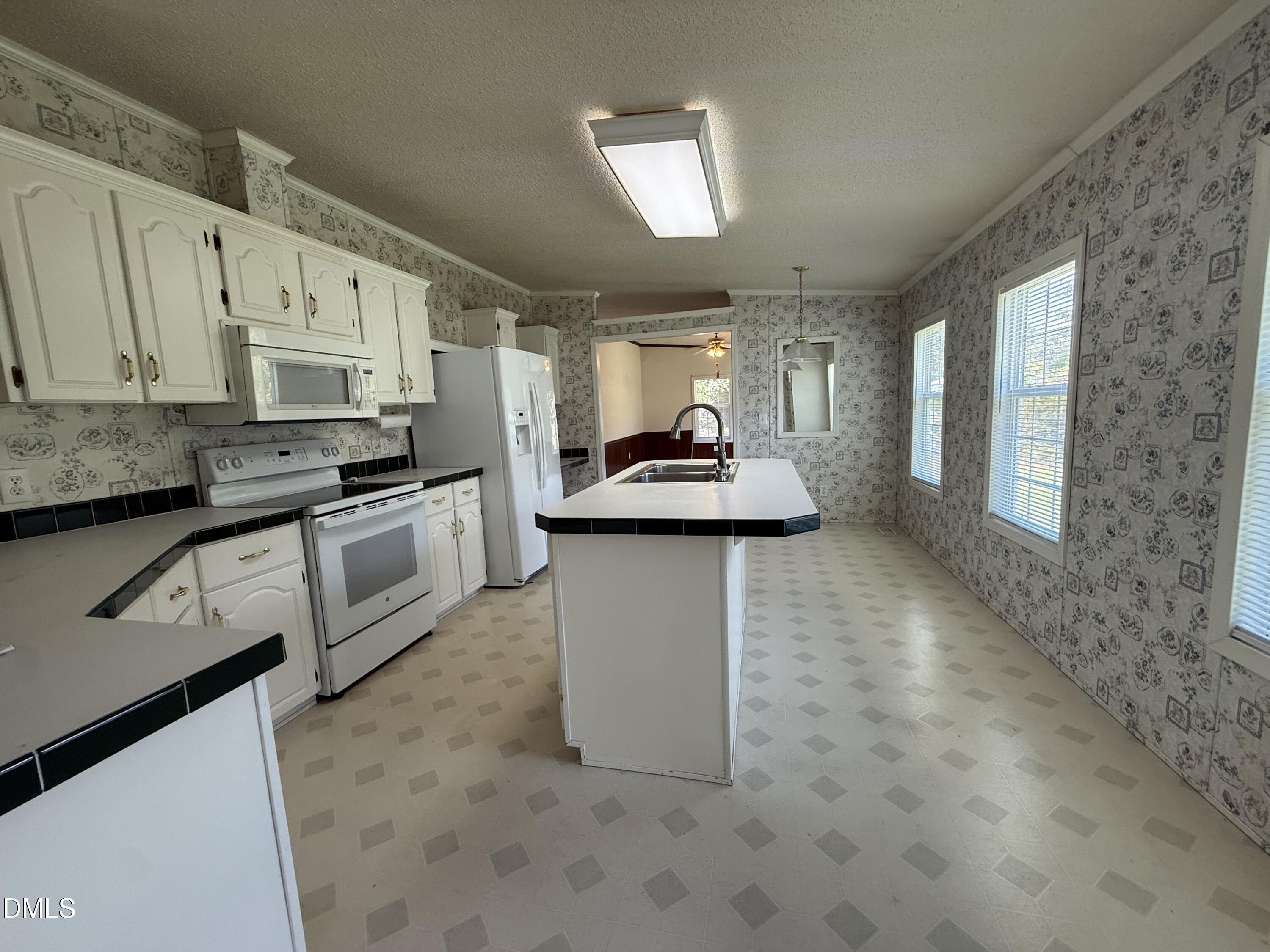Kitchen with white cabinets, patterned wallpaper, and a large island with a sink.